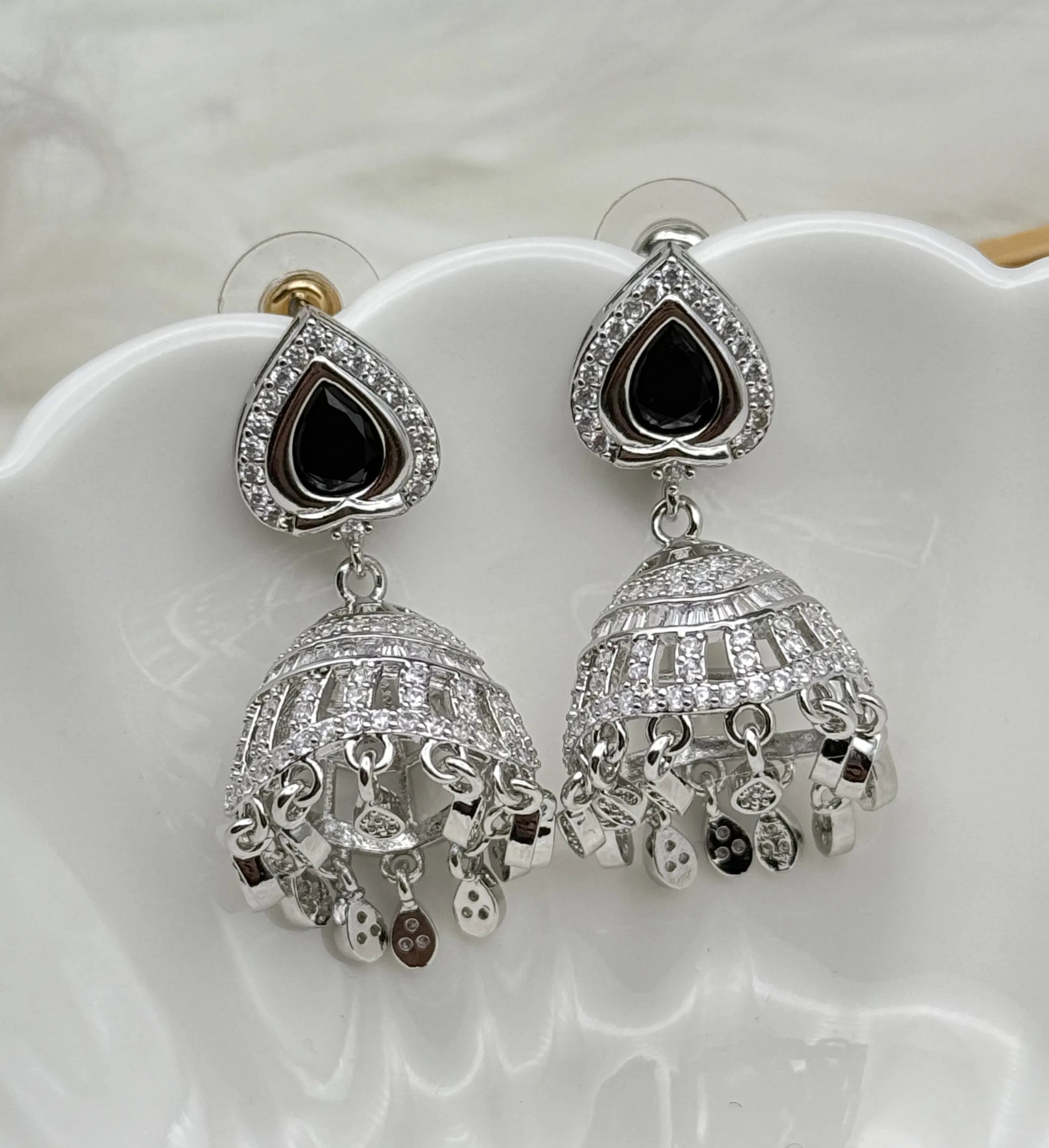 Silver American diamonds jhumka earrings with black stones on a white dish