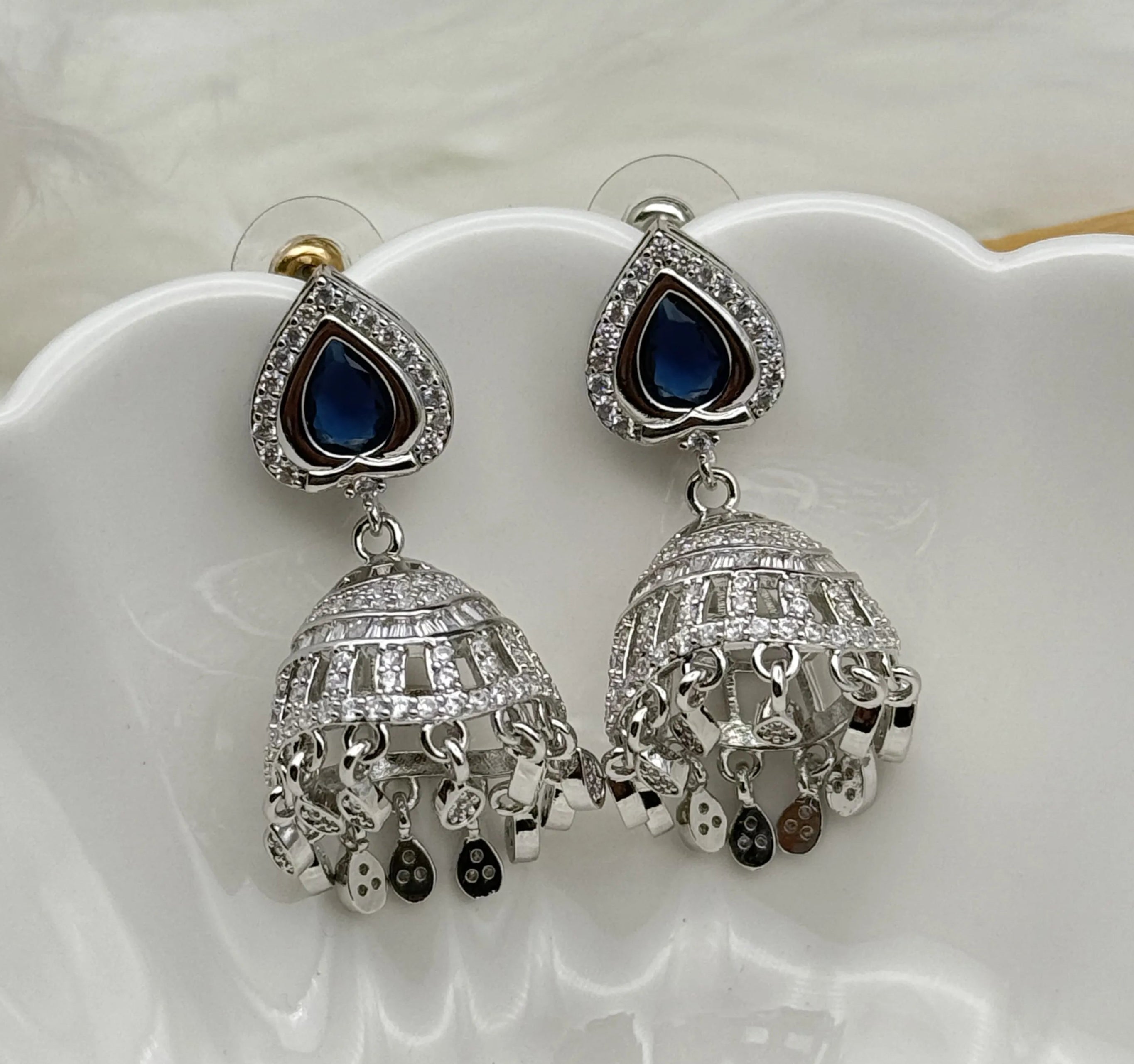 Silver American diamonds jhumka earrings with blue gemstones on a white dish