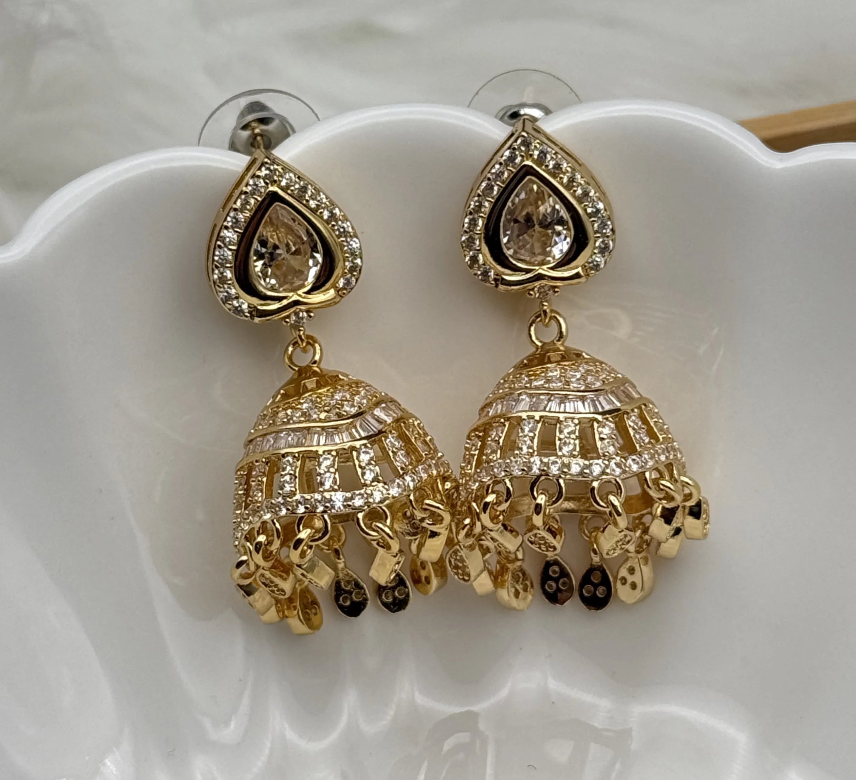 Gold plated jhumka earrings with intricate designs on a white dish