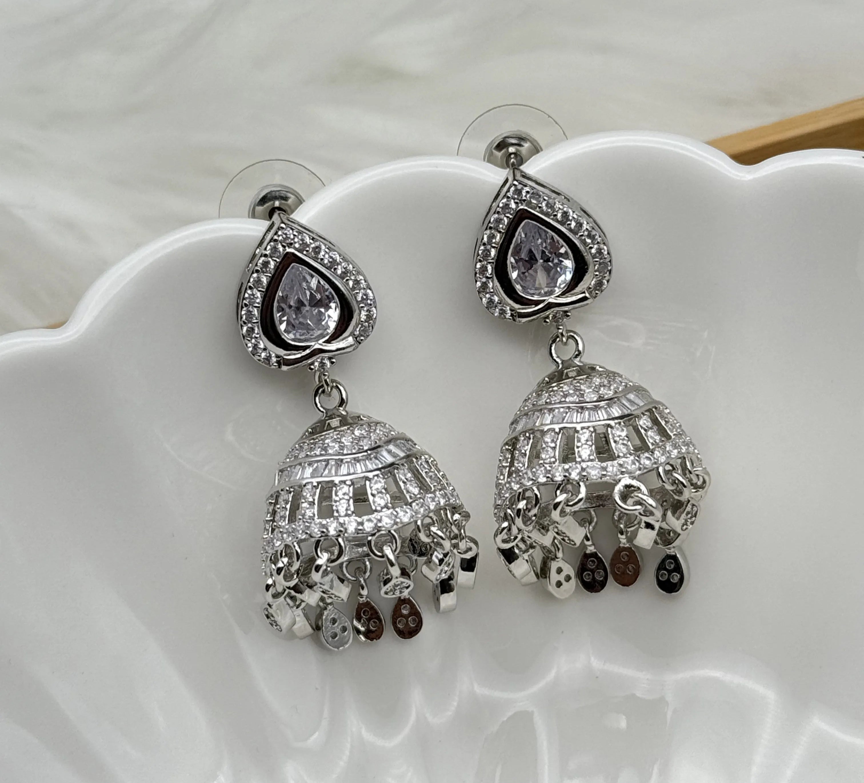 Silver American diamonds jhumka earrings with teardrop designs on a white dish