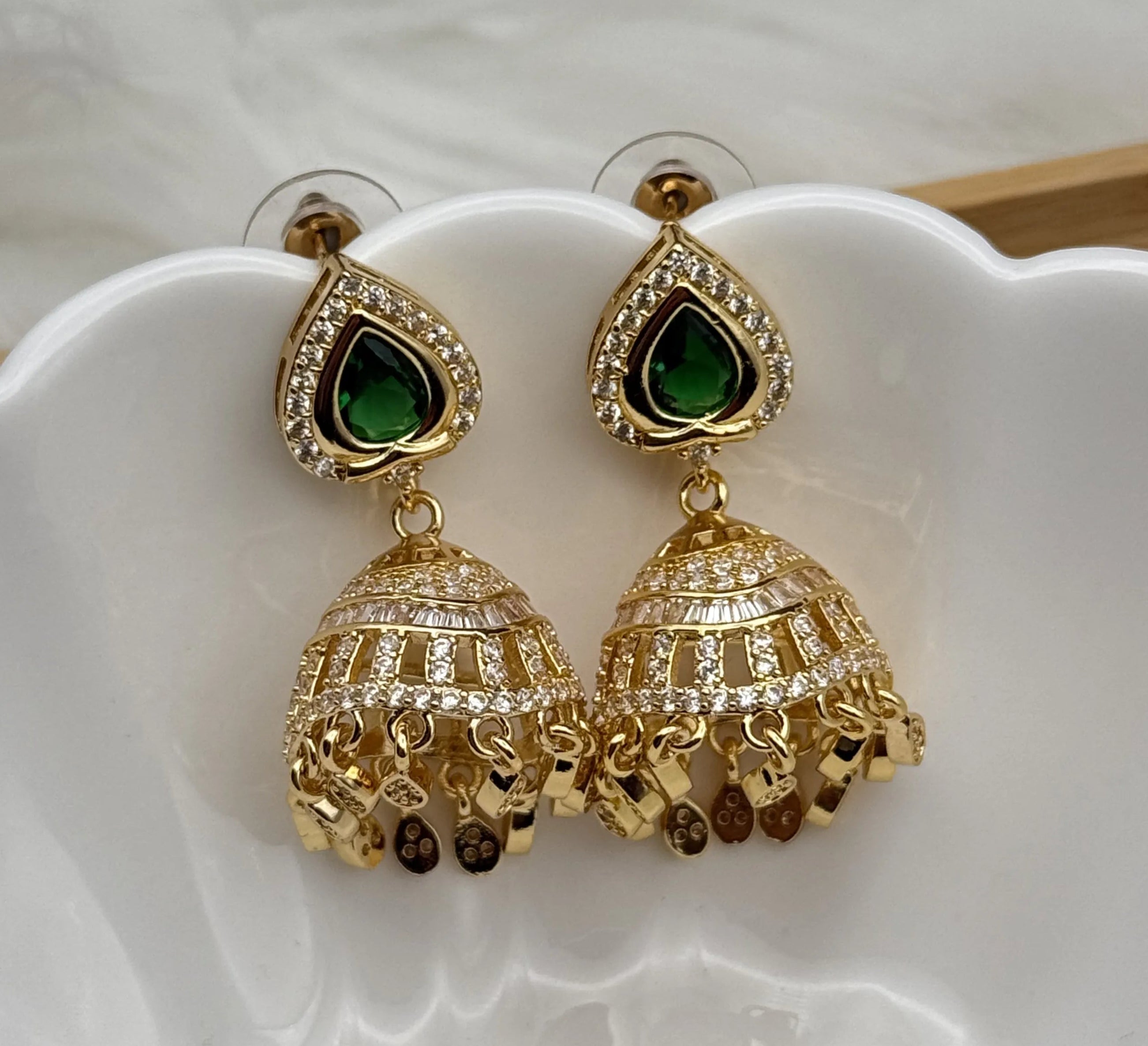 Gold plated jhumka earrings with green gemstones on a white dish
