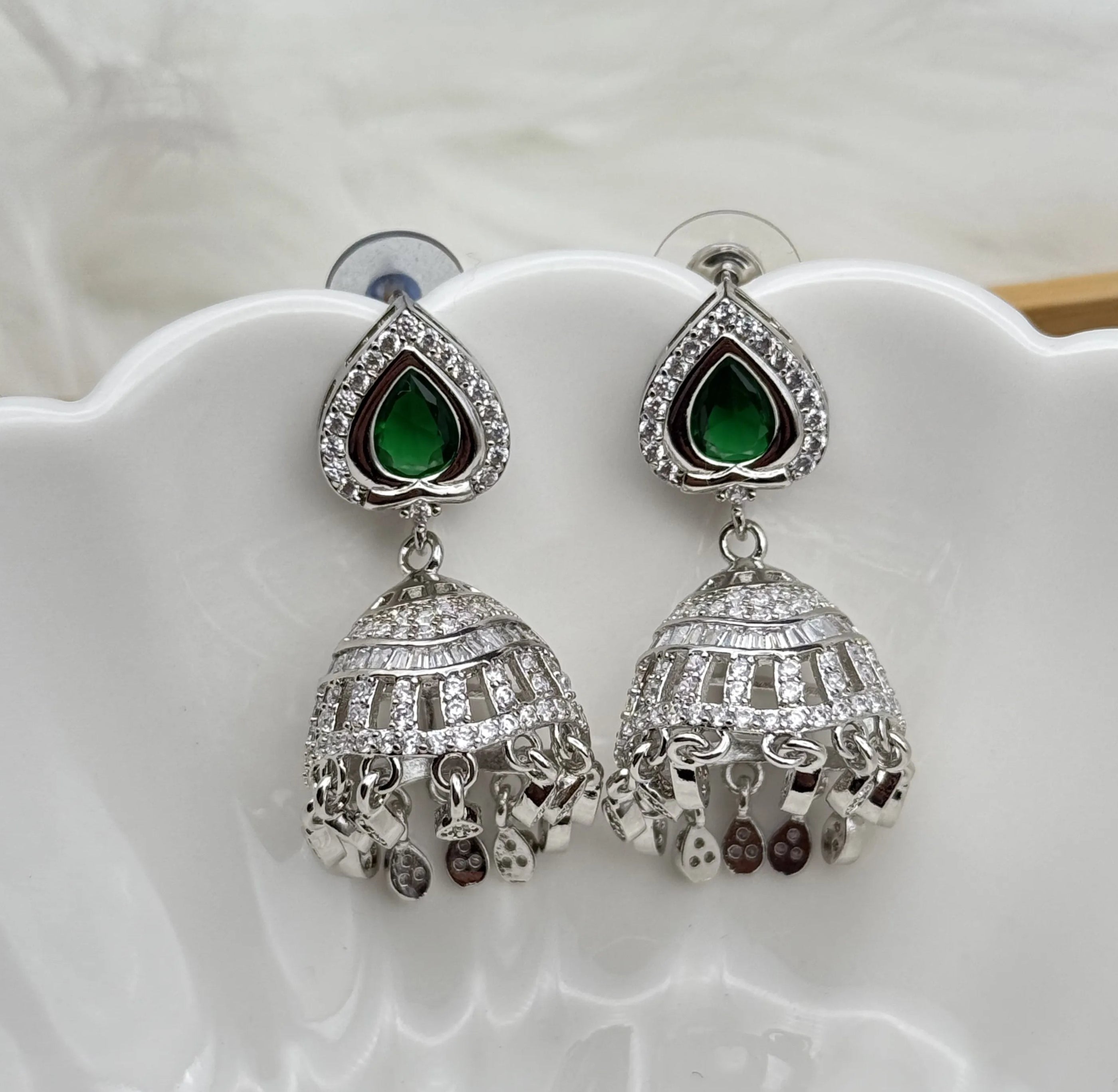 Silver American diamonds jhumka earrings with green gemstones on a white shell