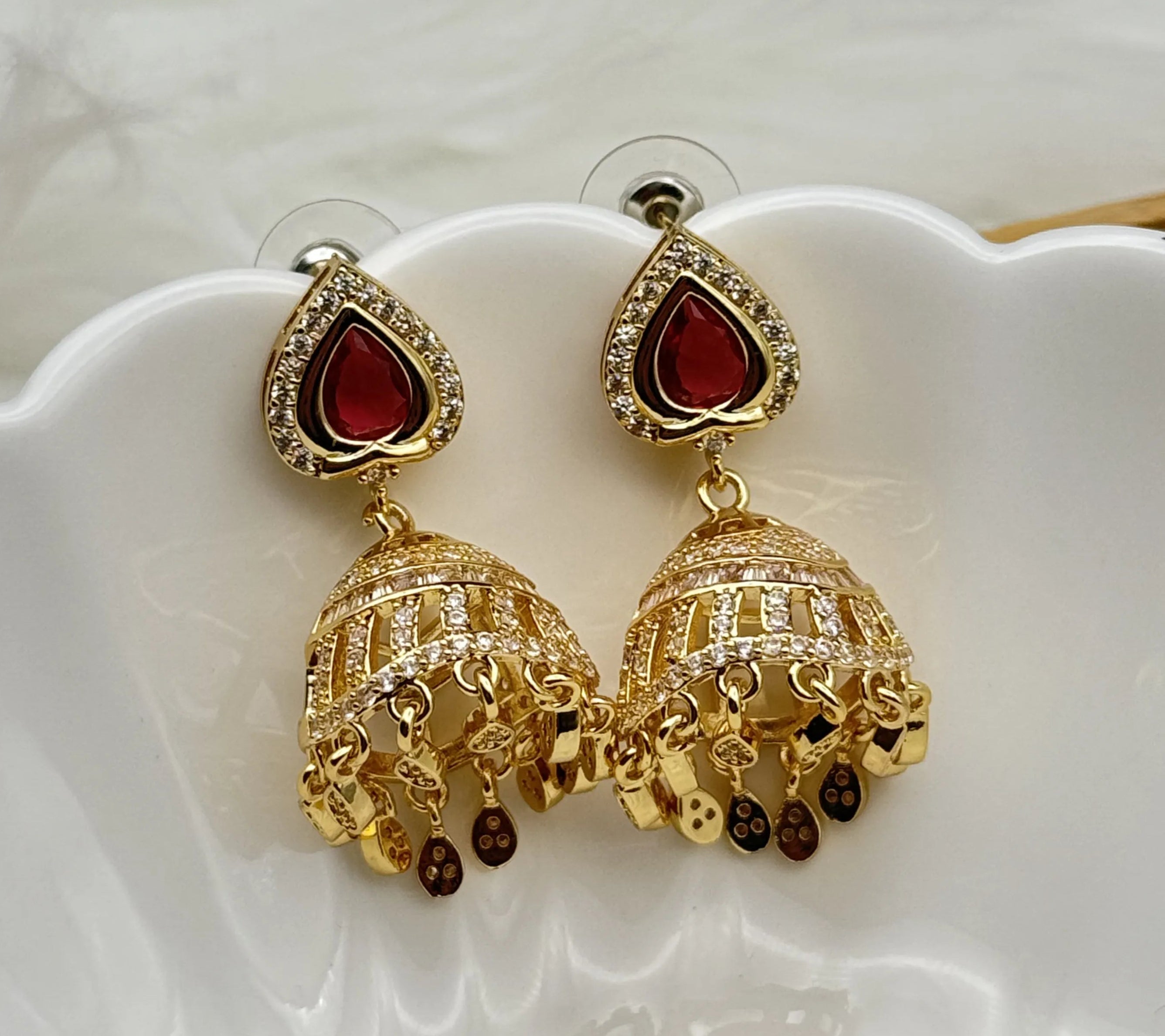 Gold plated jhumka earrings with red gemstones on a white dish