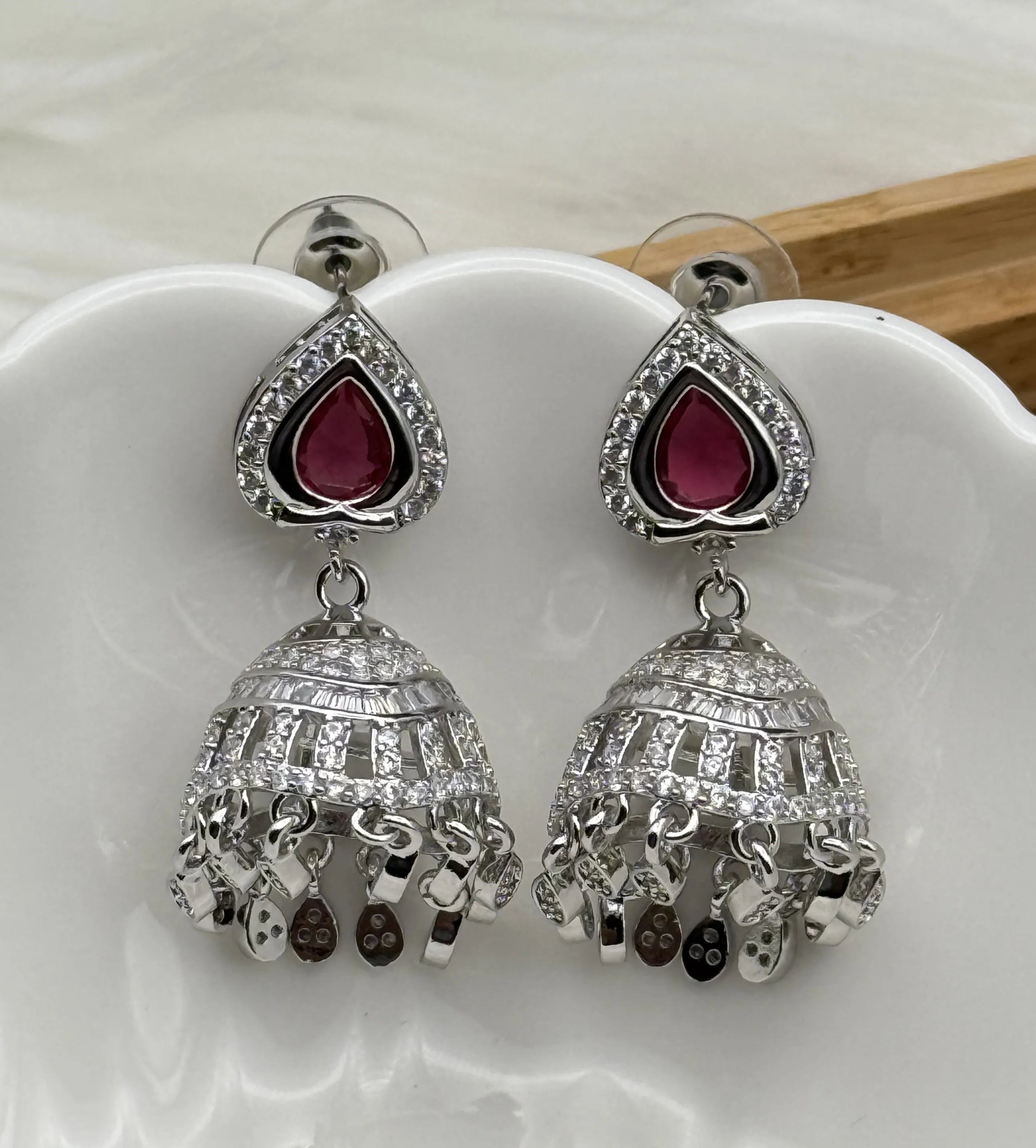 Silver American diamonds jhumka earrings with hotpink gemstones on a white dish