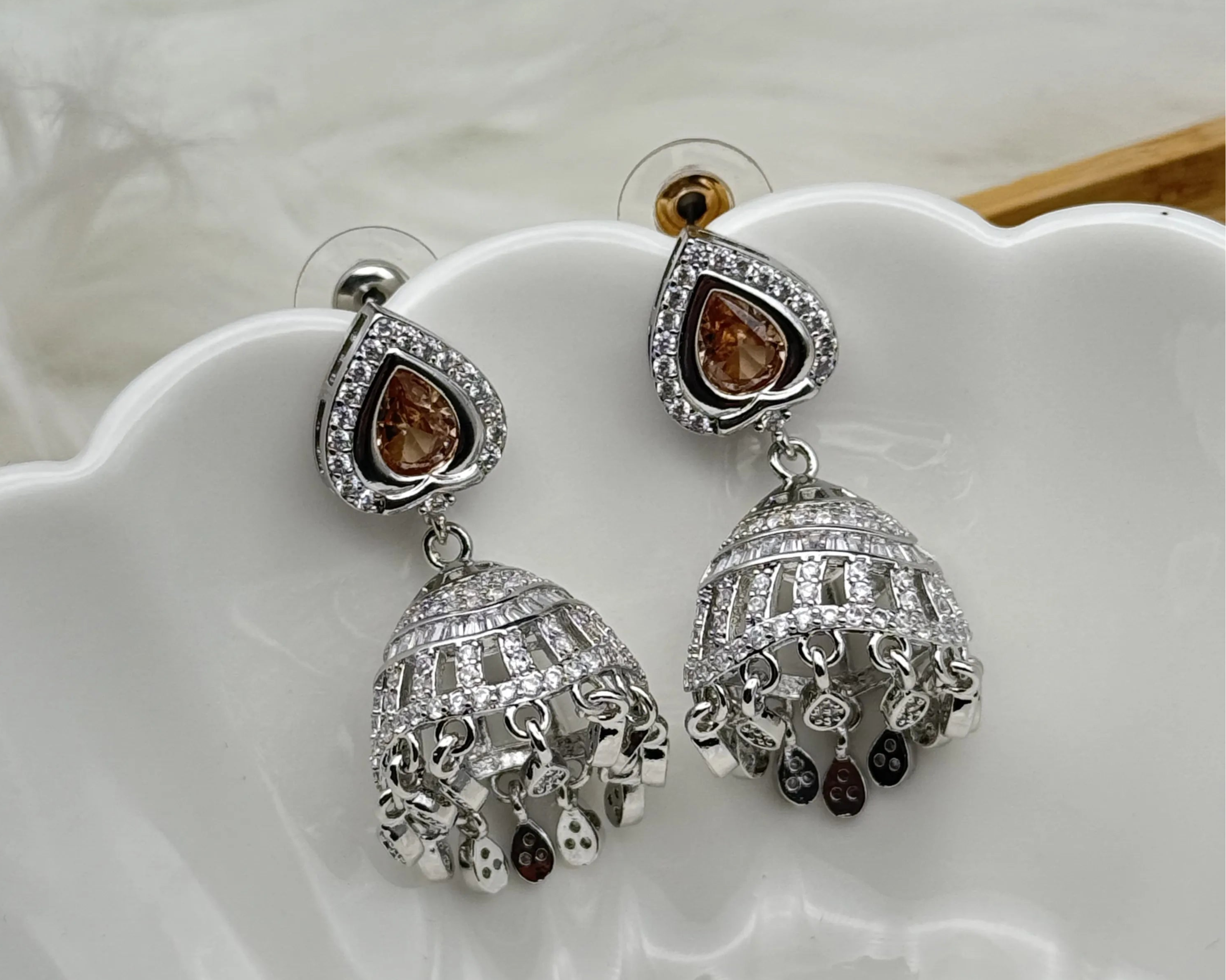 Silver American diamonds jhumka earrings with peach gemstones on a white dish