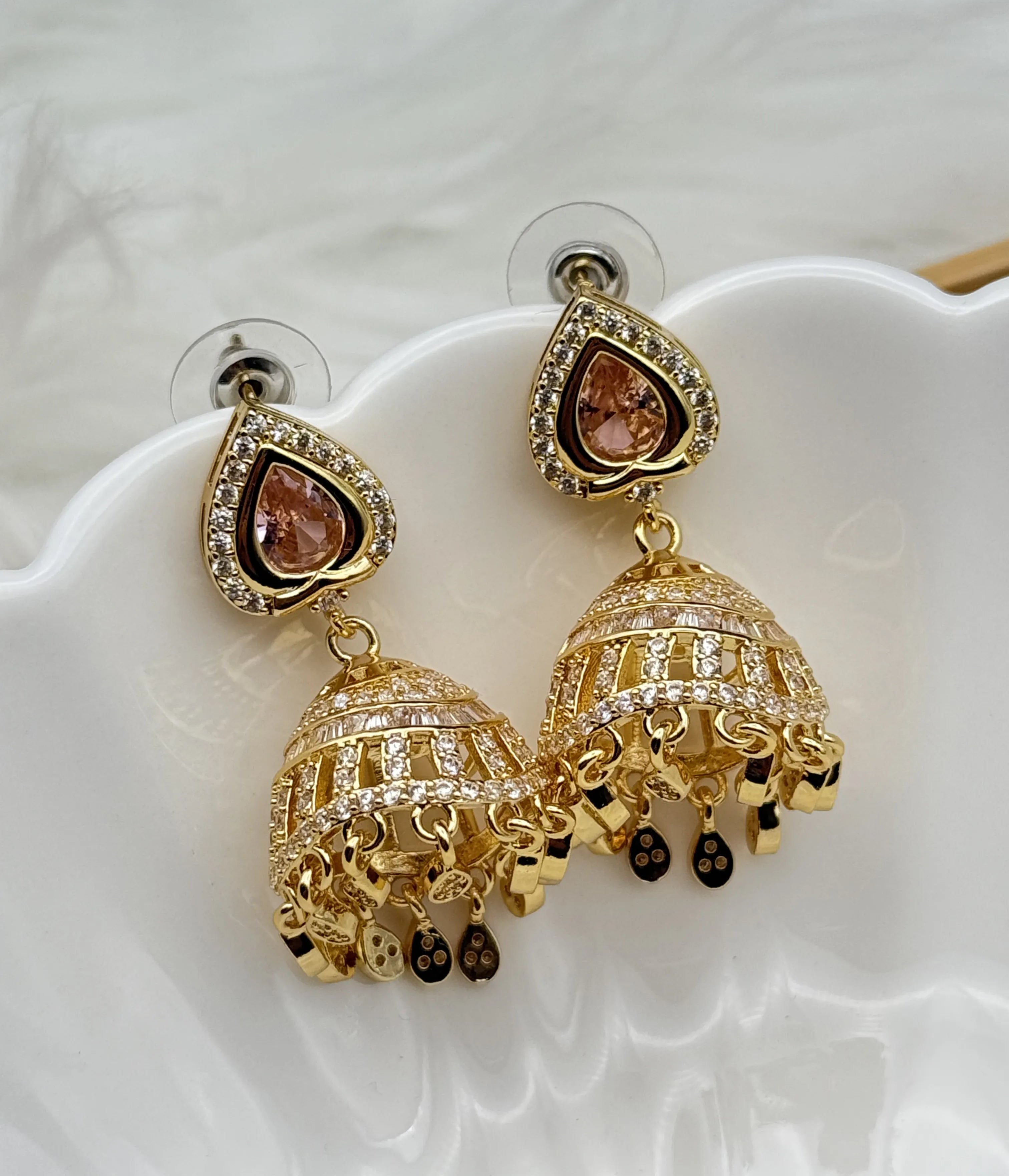 Gold plated jhumka earrings with heart-shaped stones on a white surface