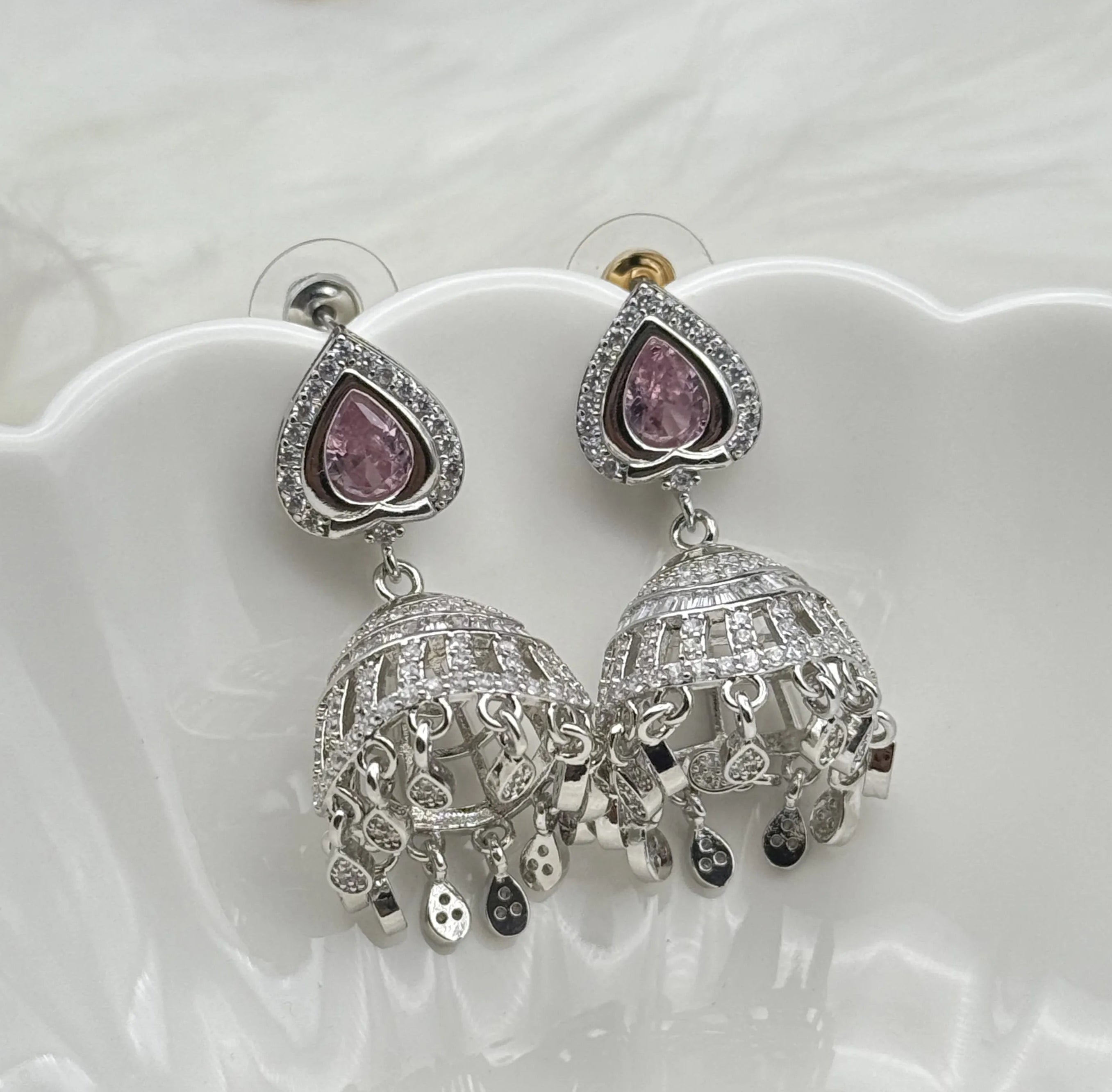 Silver American diamonds jhumka earrings with pink gemstones on a white dish