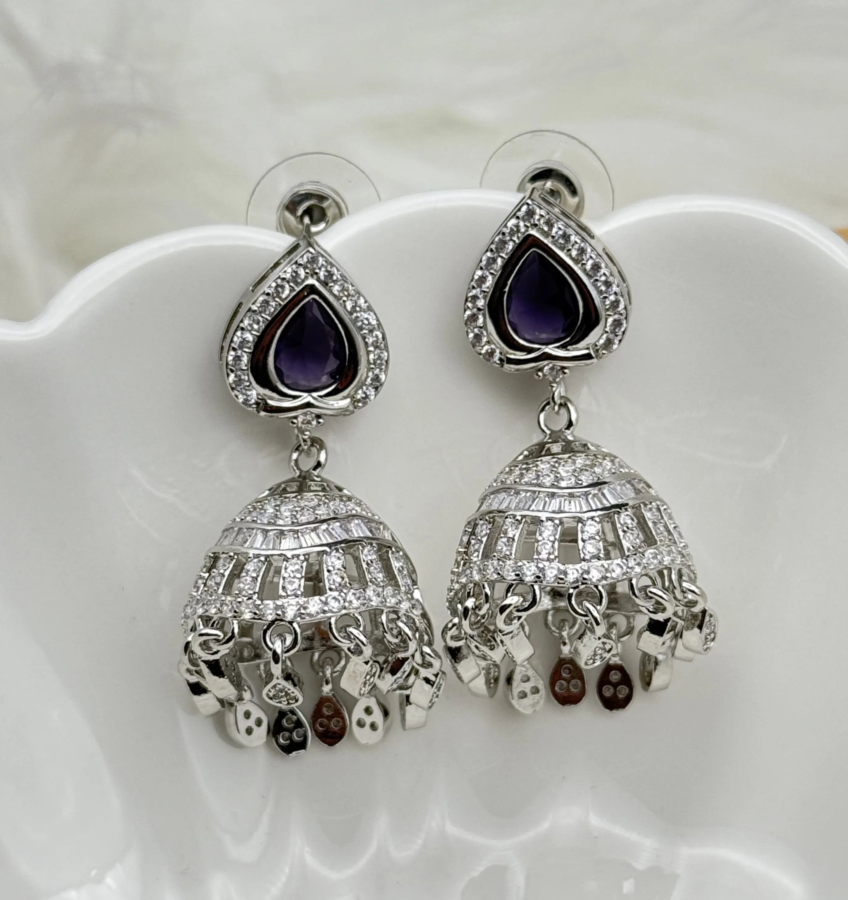 Silver American diamonds jhumka earrings with purple stones on a white dish
