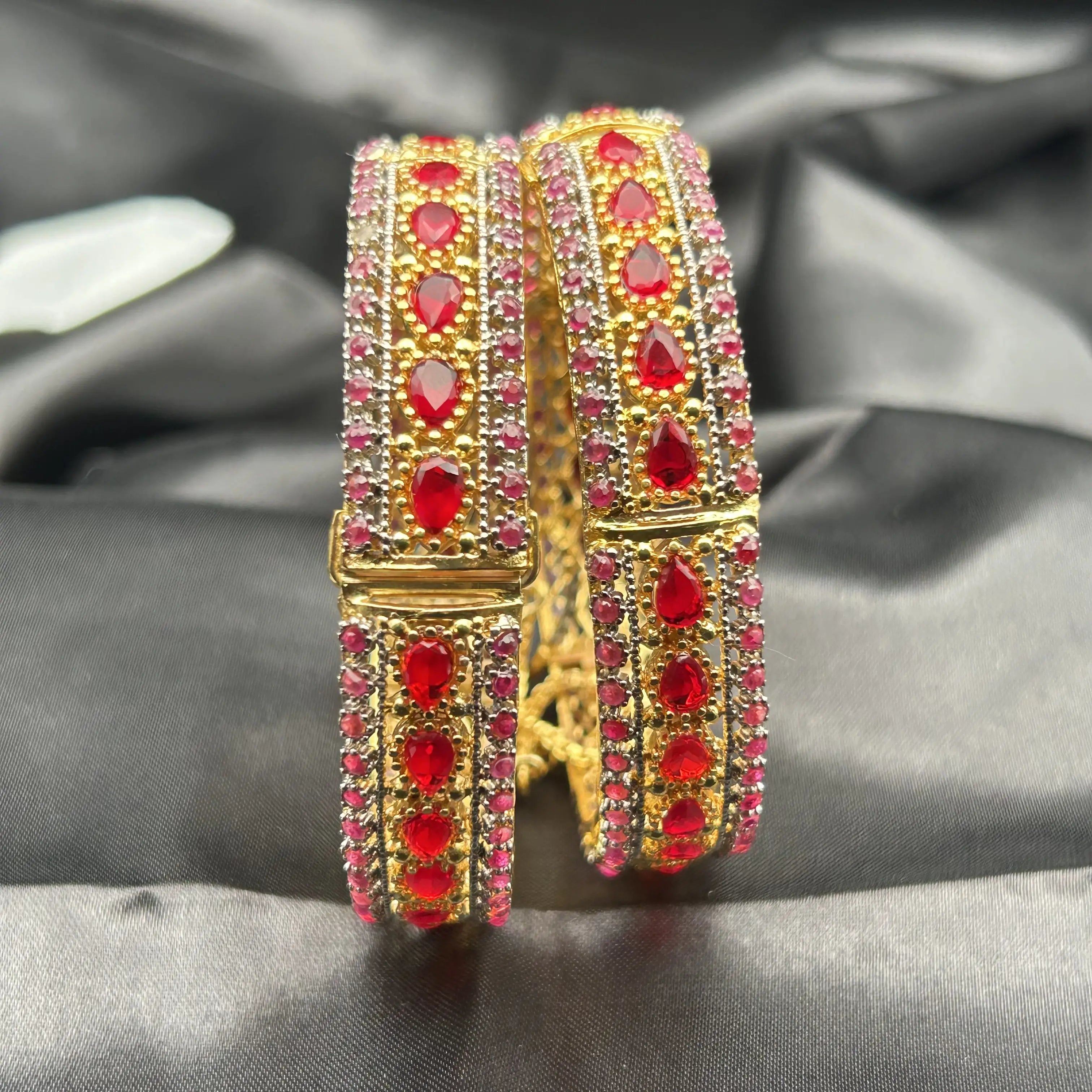 Openable gold-toned bangle pair with vibrant red and pink stones – angled close-up