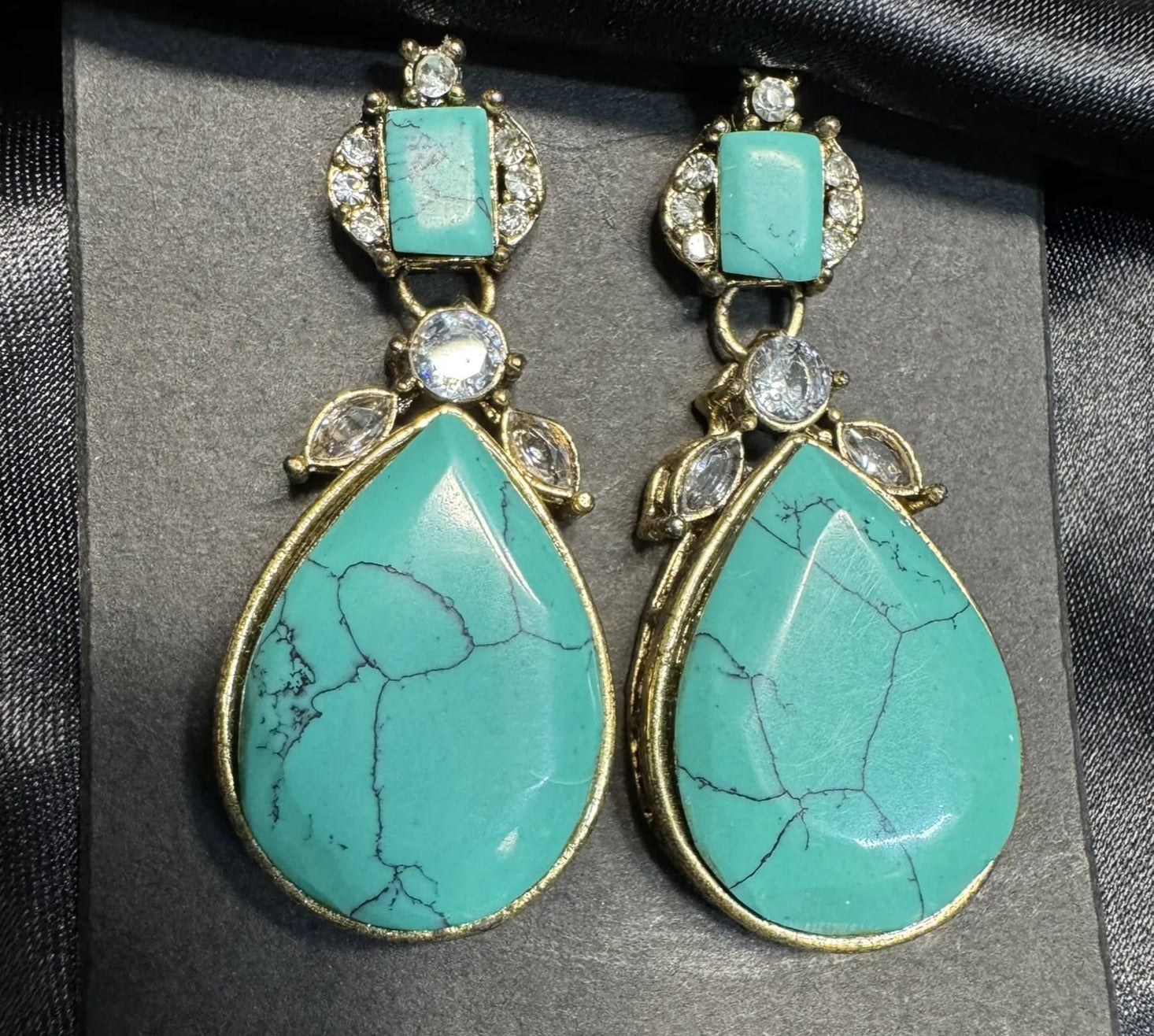 Turquoise teardrop earrings with gold accents on a black background
