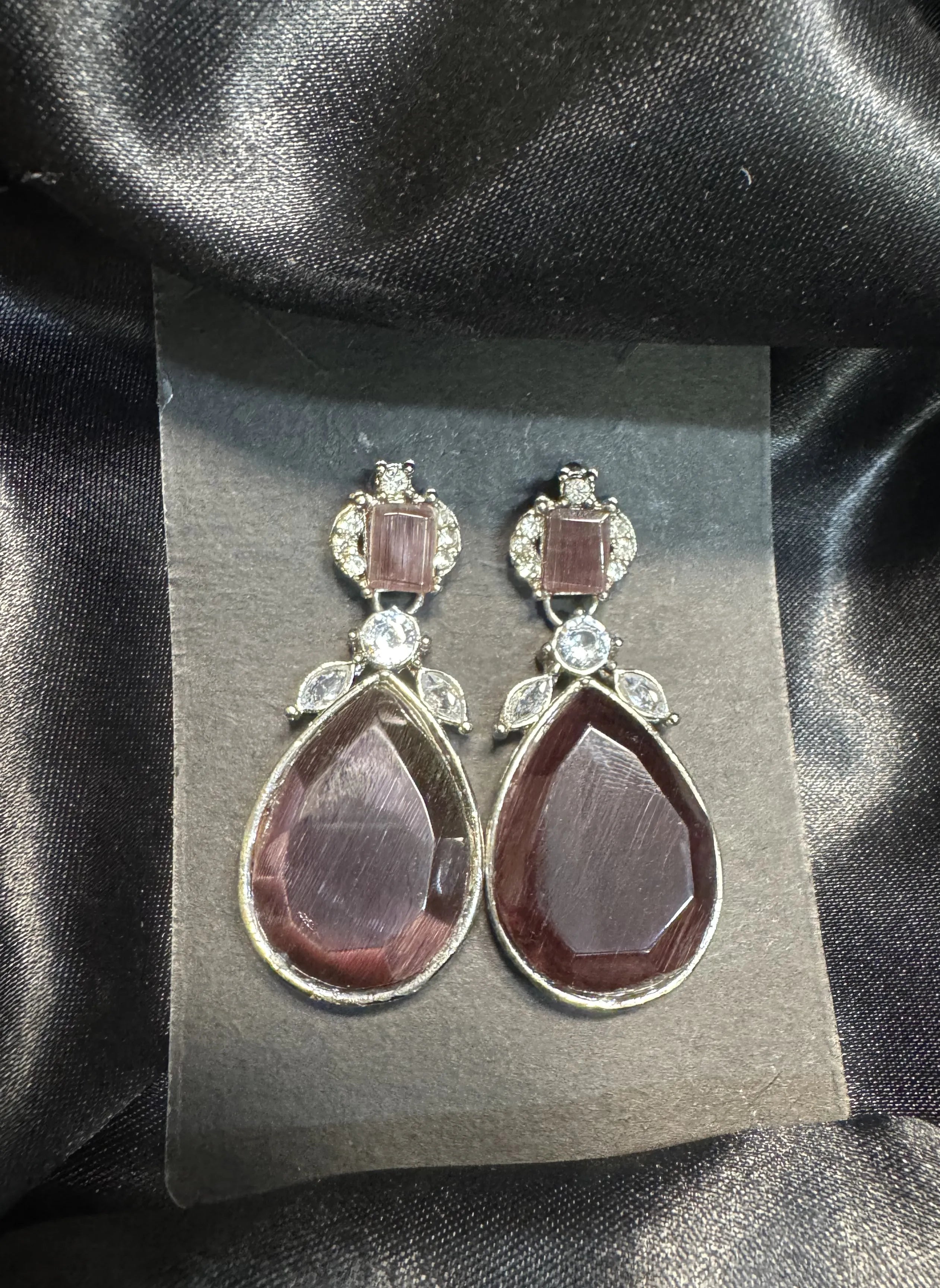 Pair of earrings on a gray card with a black satin background