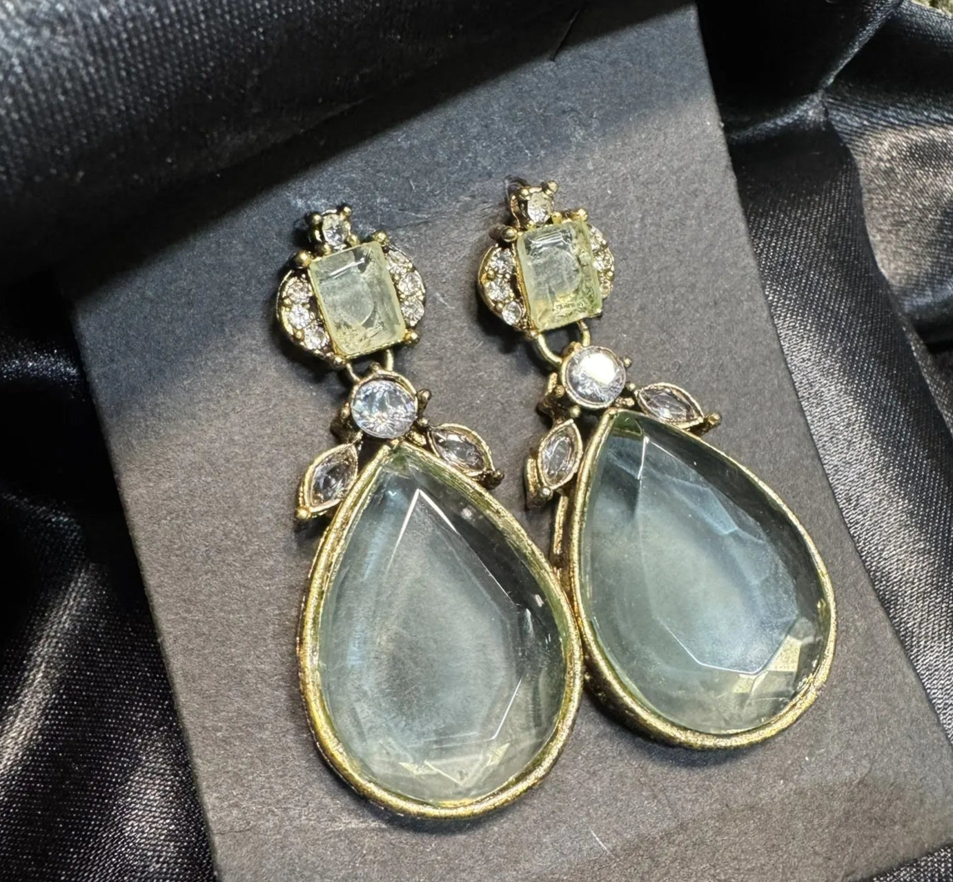 Teardrop-shaped earrings with gold and gemstone details on a black satin background