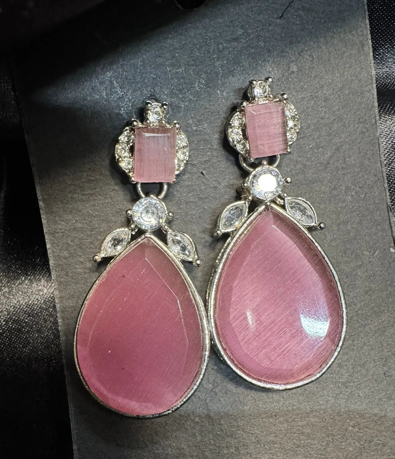 Pink teardrop earrings with silver and gemstone details on a dark background