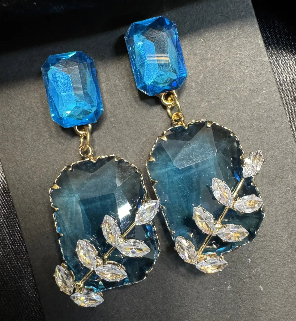 Blue gemstone earrings with leaf designs on a black background