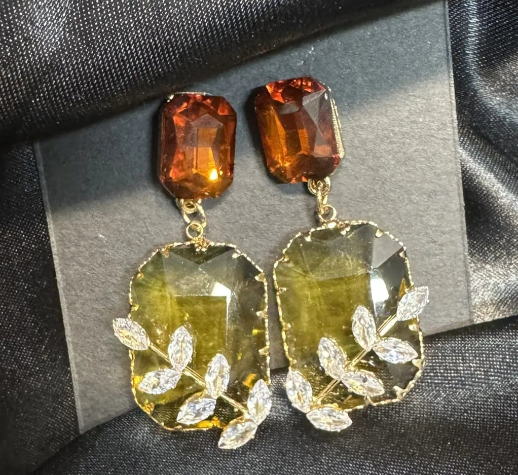 Pair of earrings with orange and clear stones on a dark fabric background