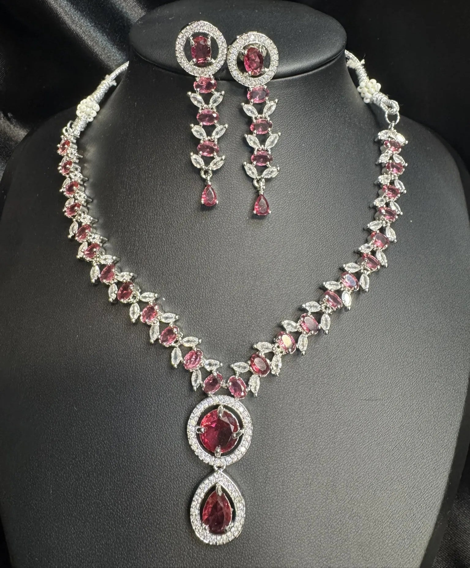 Necklace and earrings set with hot pink gemstones on a black background