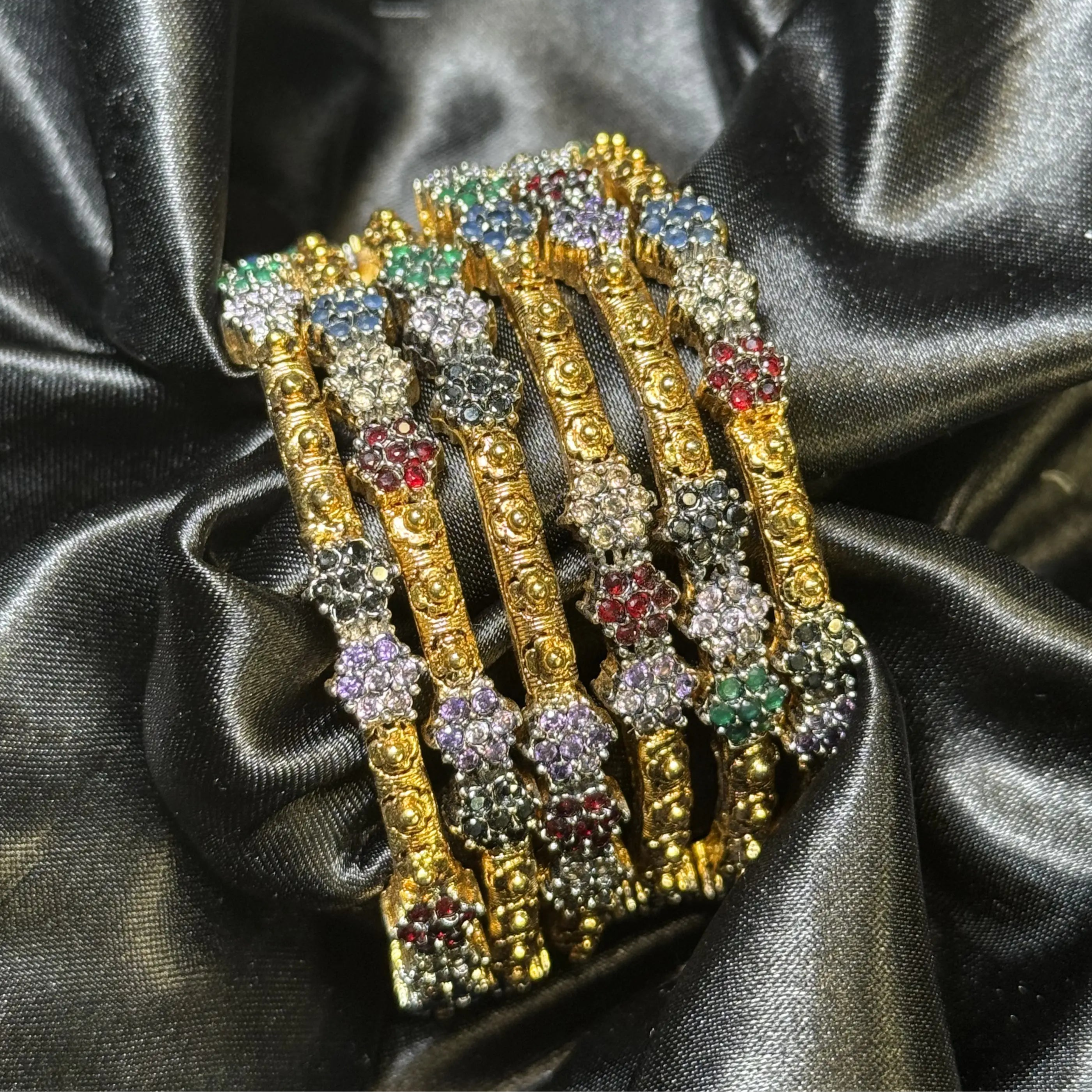 Set of 6 gold plated bangles with multicolor stone clusters on black satin