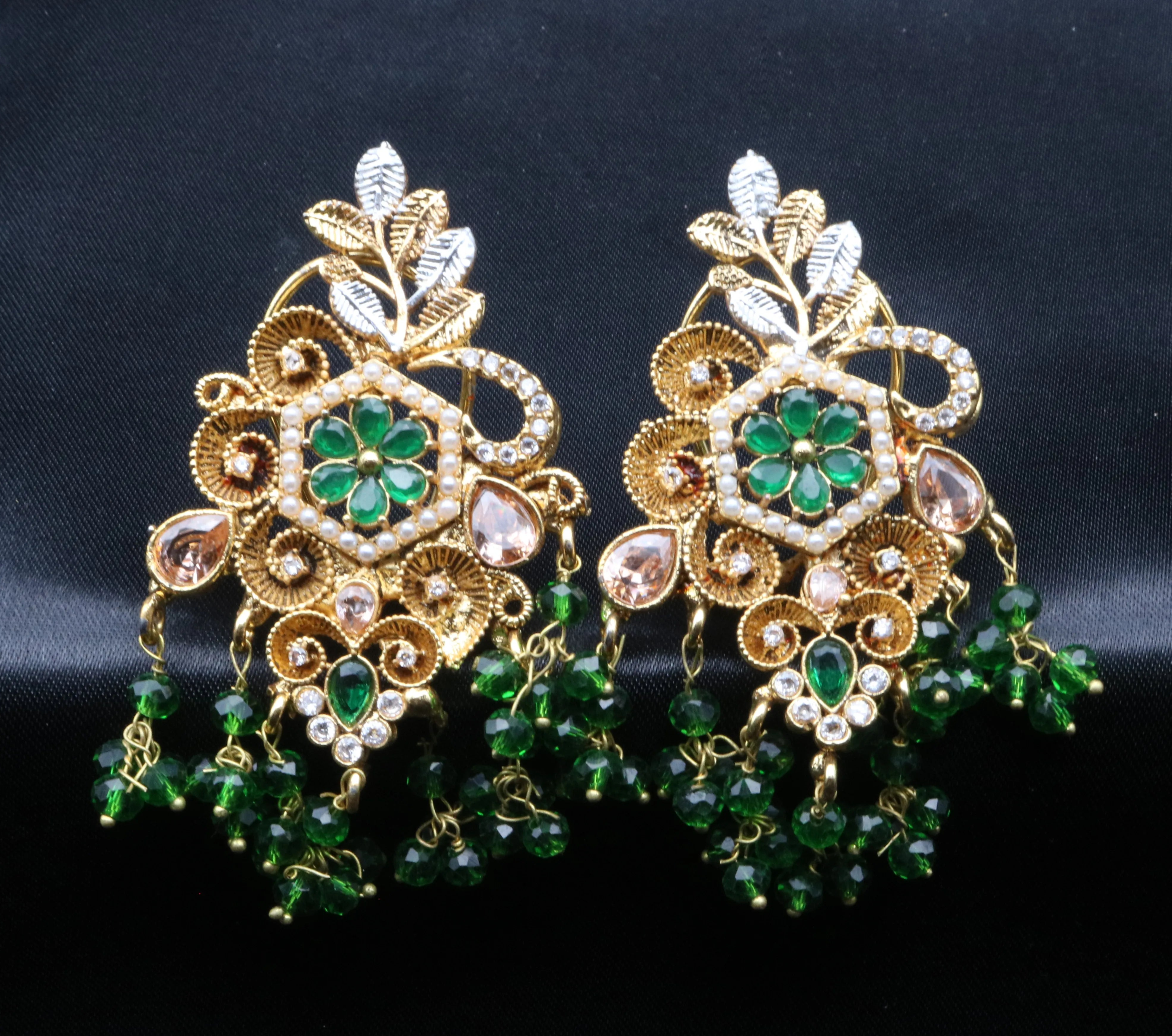 Pair of ornate earrings with green gemstones on a black background