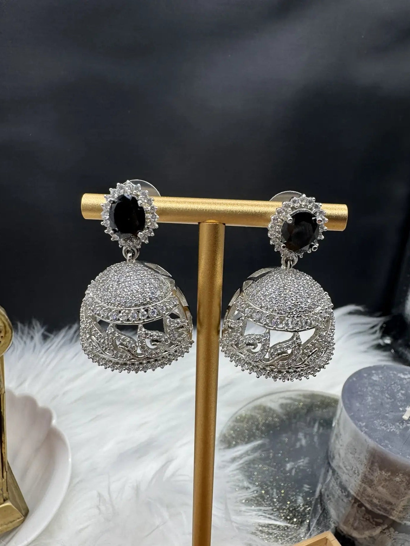 American diamonds and nano zarcon Pakistani style jhumka earrings with black gemstones and silver base on a gold stand against a dark background. Jarao based design 