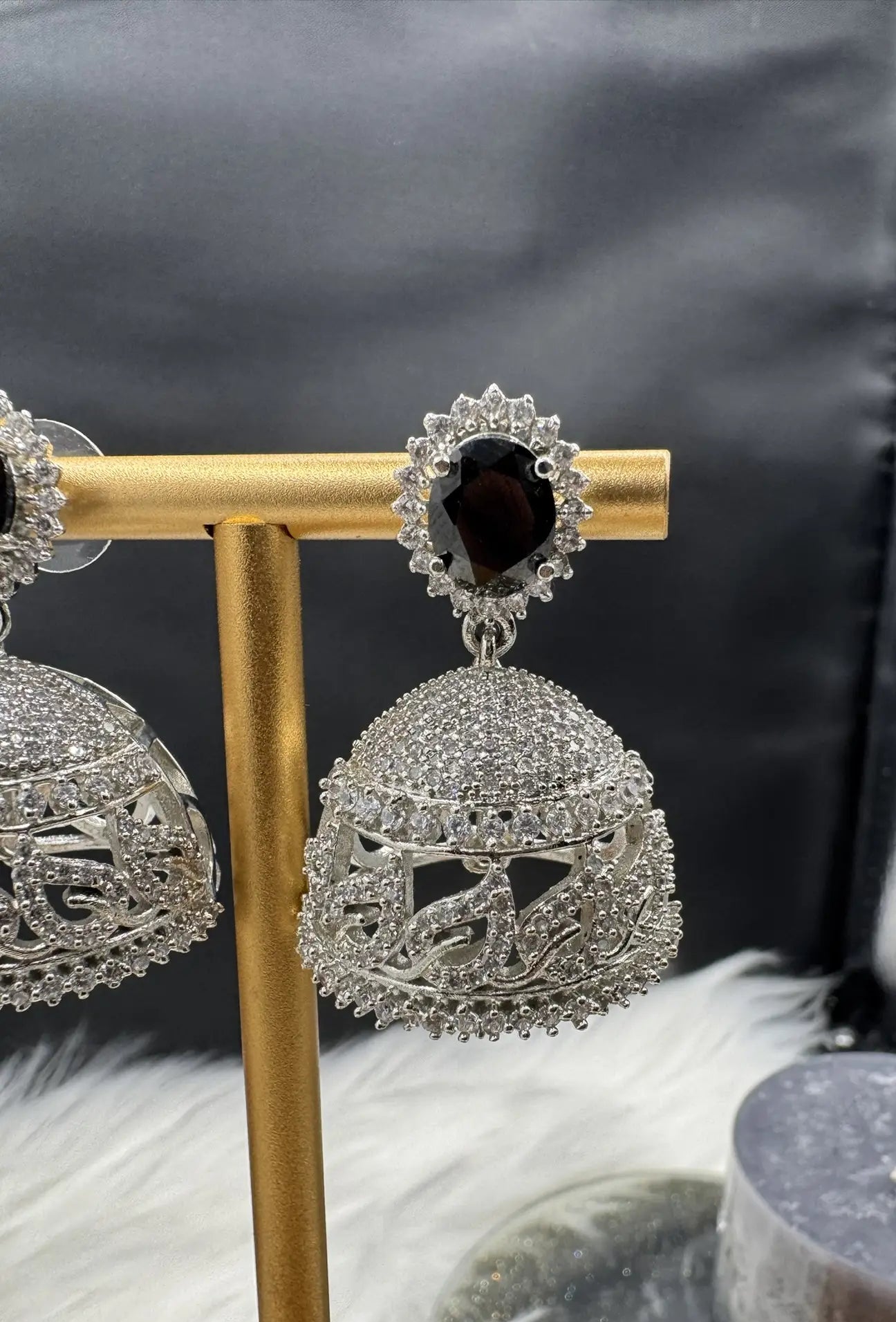 right side angle of American diamonds and nano zarcon Pakistani style jhumka earrings with black gemstones and silver base on a gold stand against a dark background. Jarao based design 