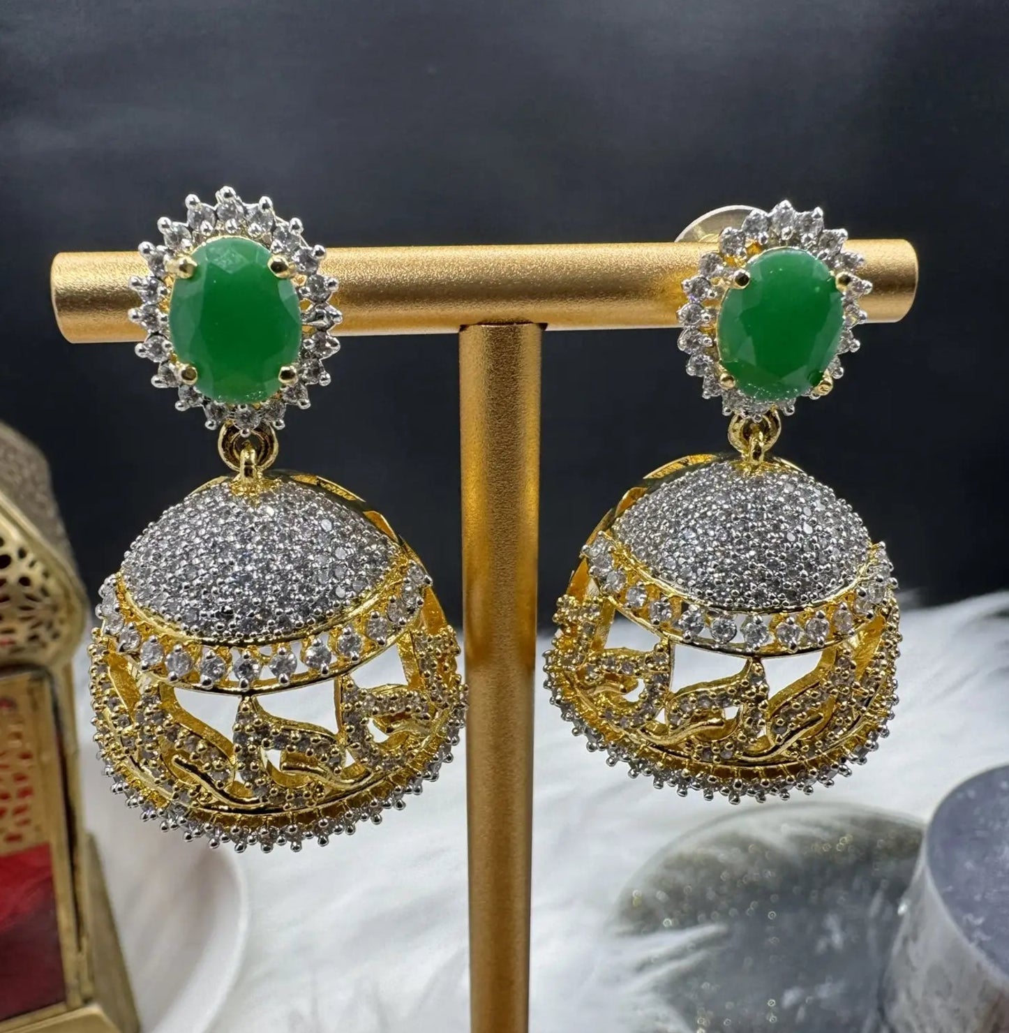 Goldplated and nano zarcon Pakistani style jhumka earrings with green gemstones on a gold stand against a dark background. Jarao based design 