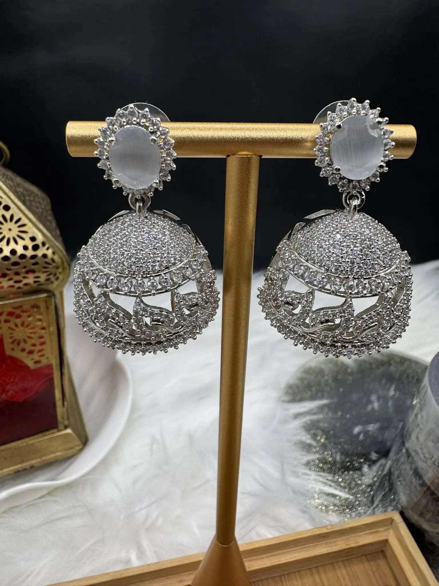 American diamonds and nano zarcon Pakistani style jhumka earrings with grey gemstones and silver base on a gold stand against a dark background. Jarao based design 