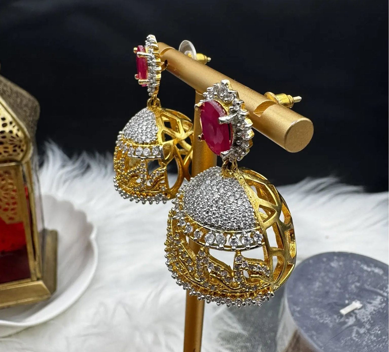 side angle of goldplated and nano zarcon Pakistani style jhumka earrings with hotpink gemstones on a gold stand against a dark background. Jarao based design 