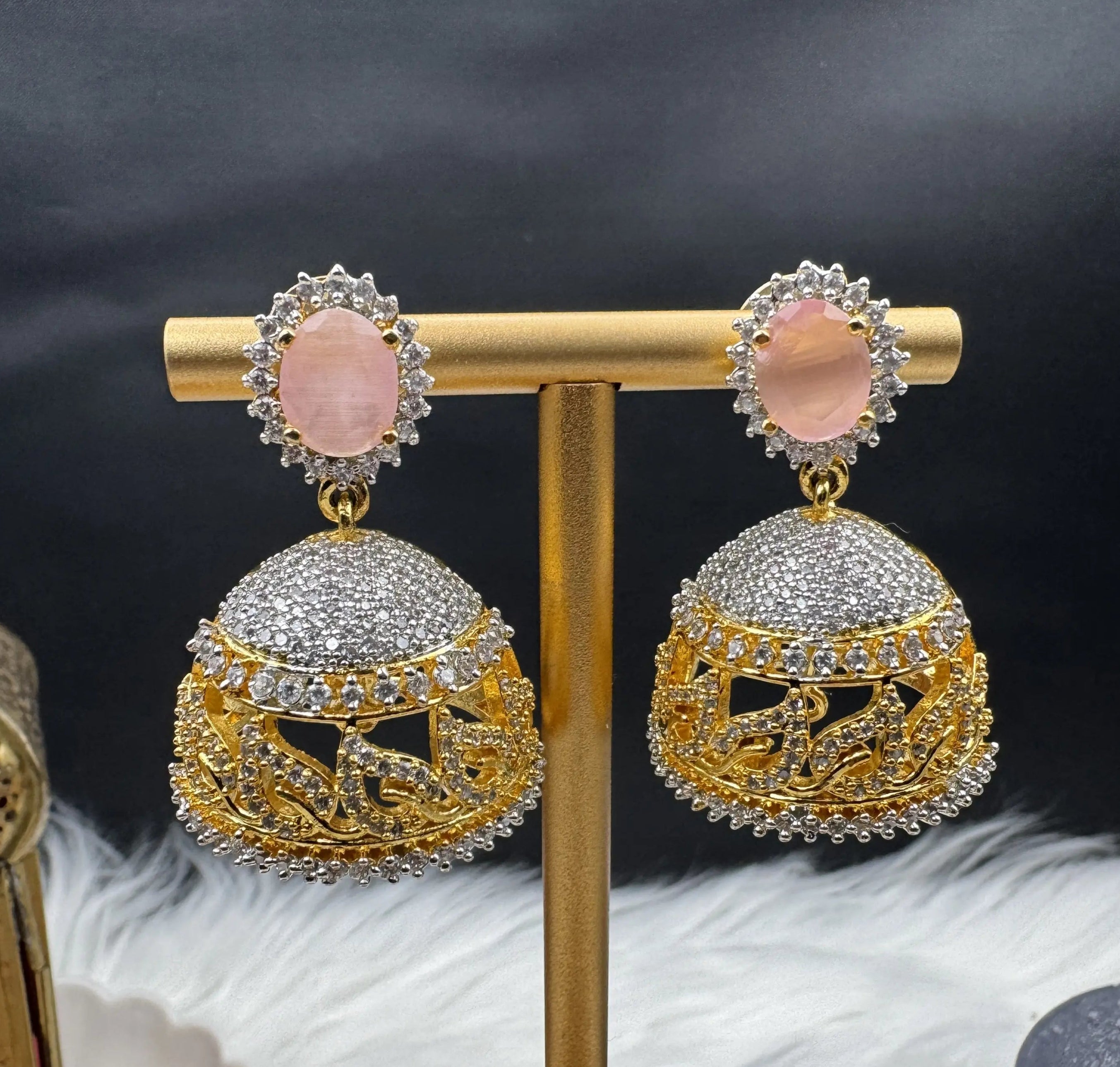 Goldplated and nano zarcon Pakistani style jhumka earrings with pink gemstones on a gold stand against a dark background. Jarao based design 
