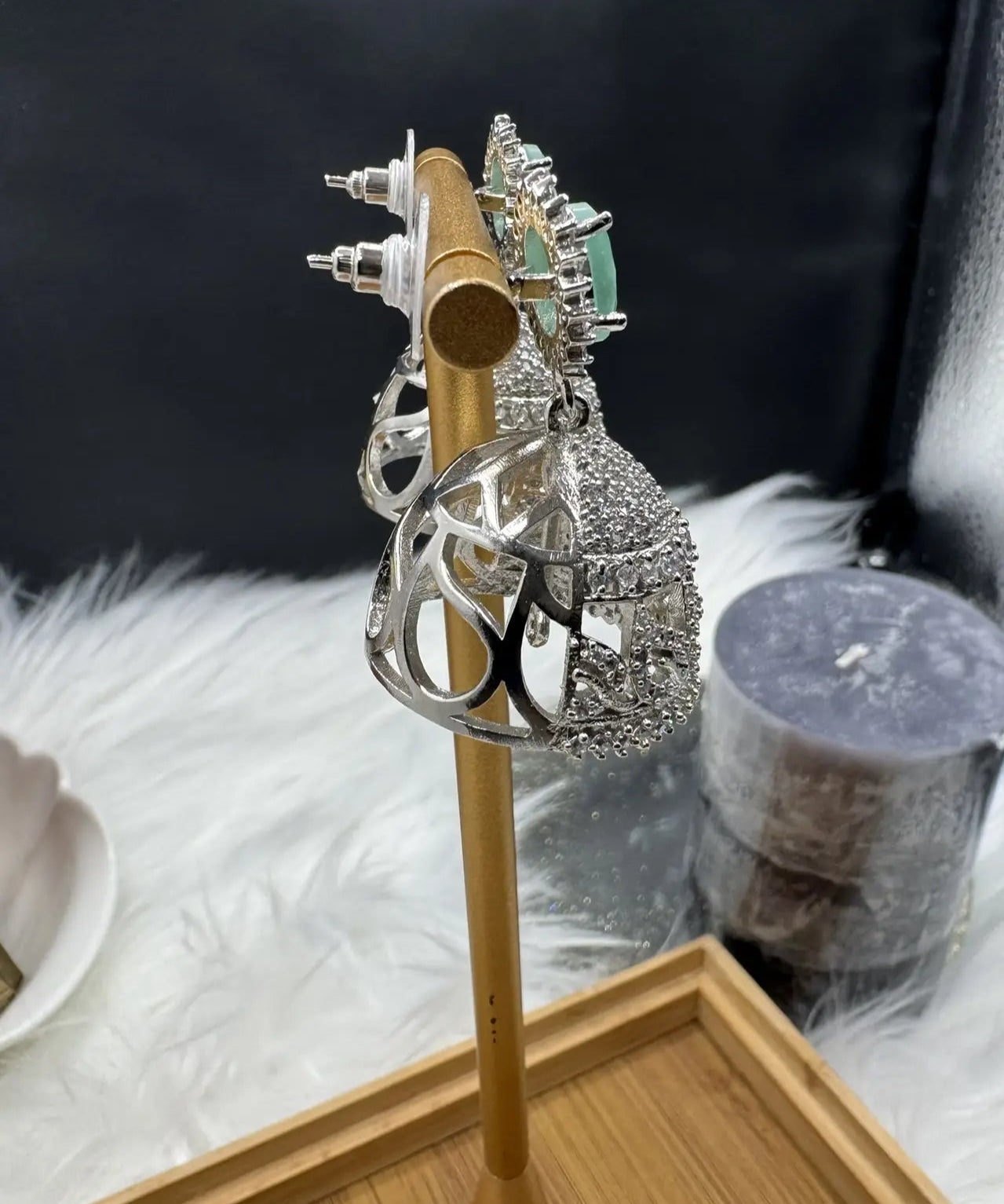 side view of American diamonds and nano zarcon Pakistani style jhumka earrings with teal gemstones and silver base on a gold stand against a dark background. Jarao based design 