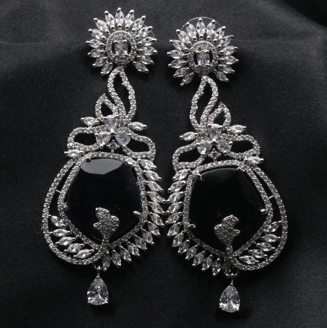 Pair of ornate American diamonds earrings with blue stones and silver detailing on a dark background