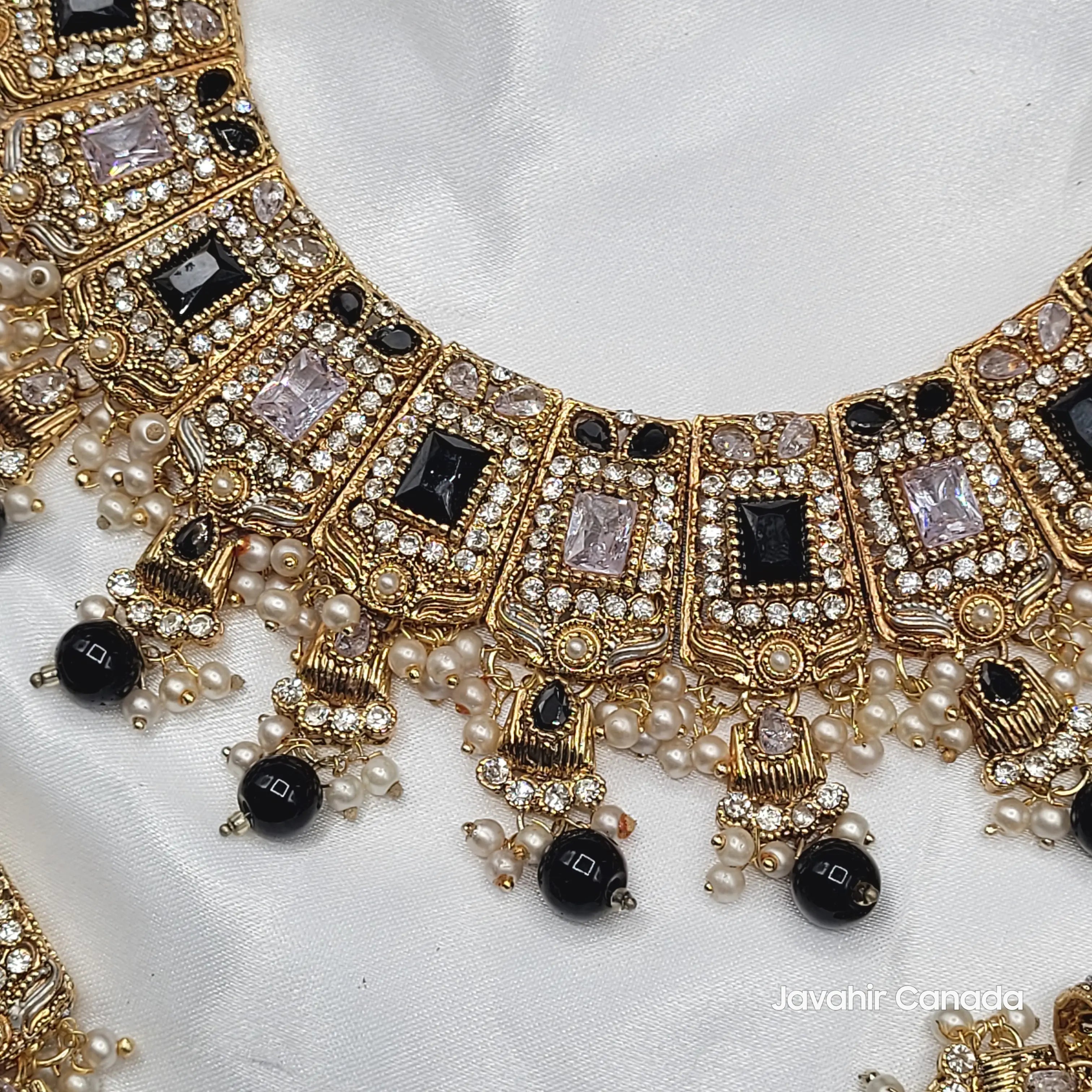 Ornate necklace with gold, black, and pearl details on a white fabric background