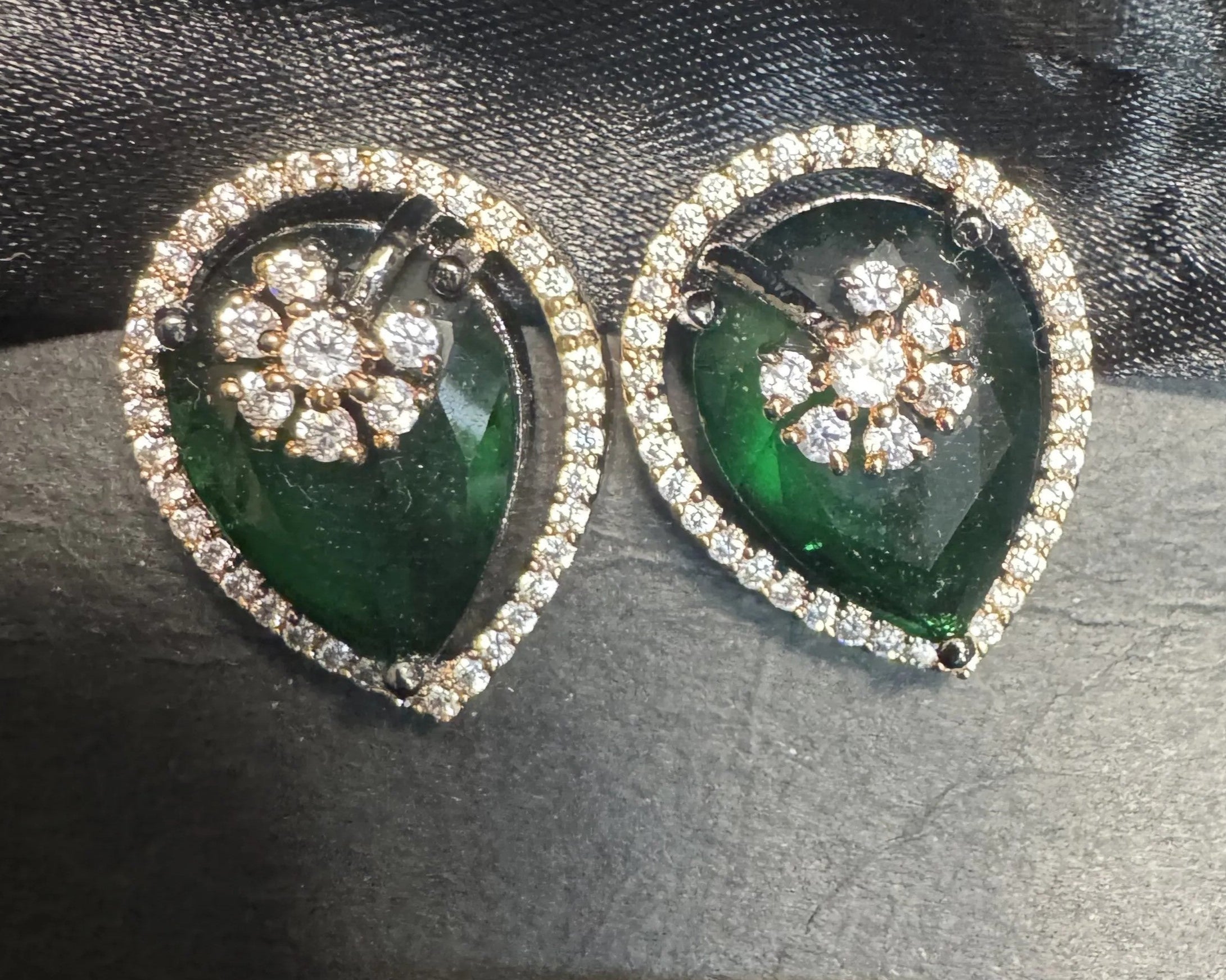 Pair of green teardrop earrings with American diamond stones on a dark textured background