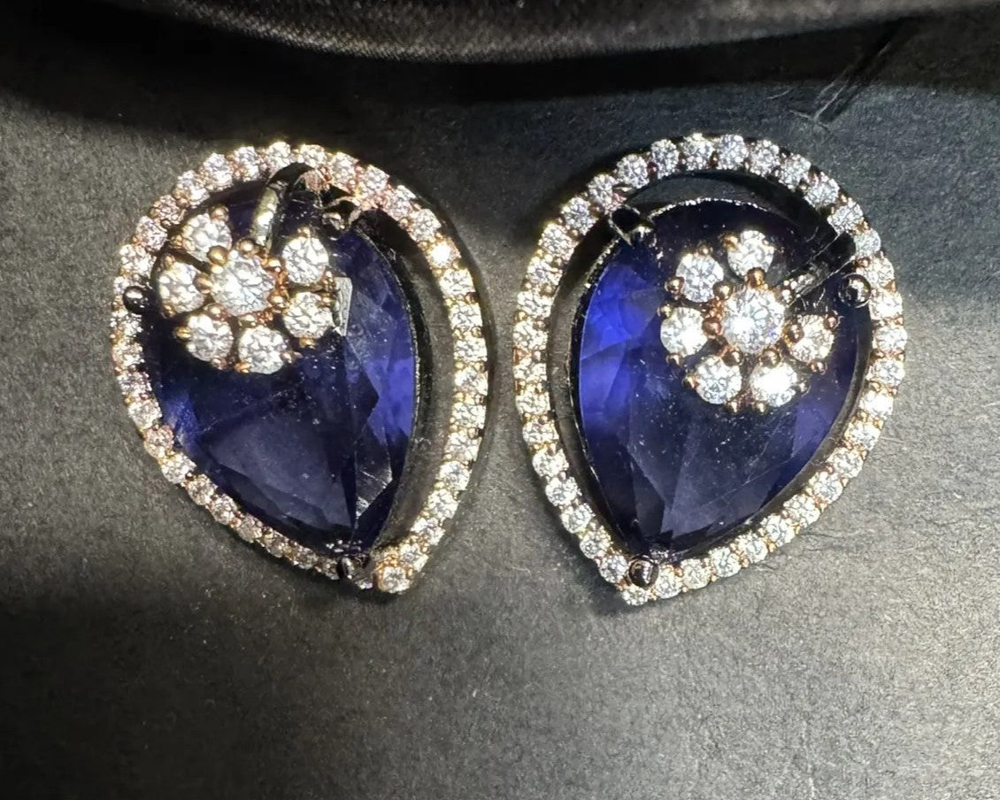 Pair of earrings with blue gemstones and American diamond stones on a dark background