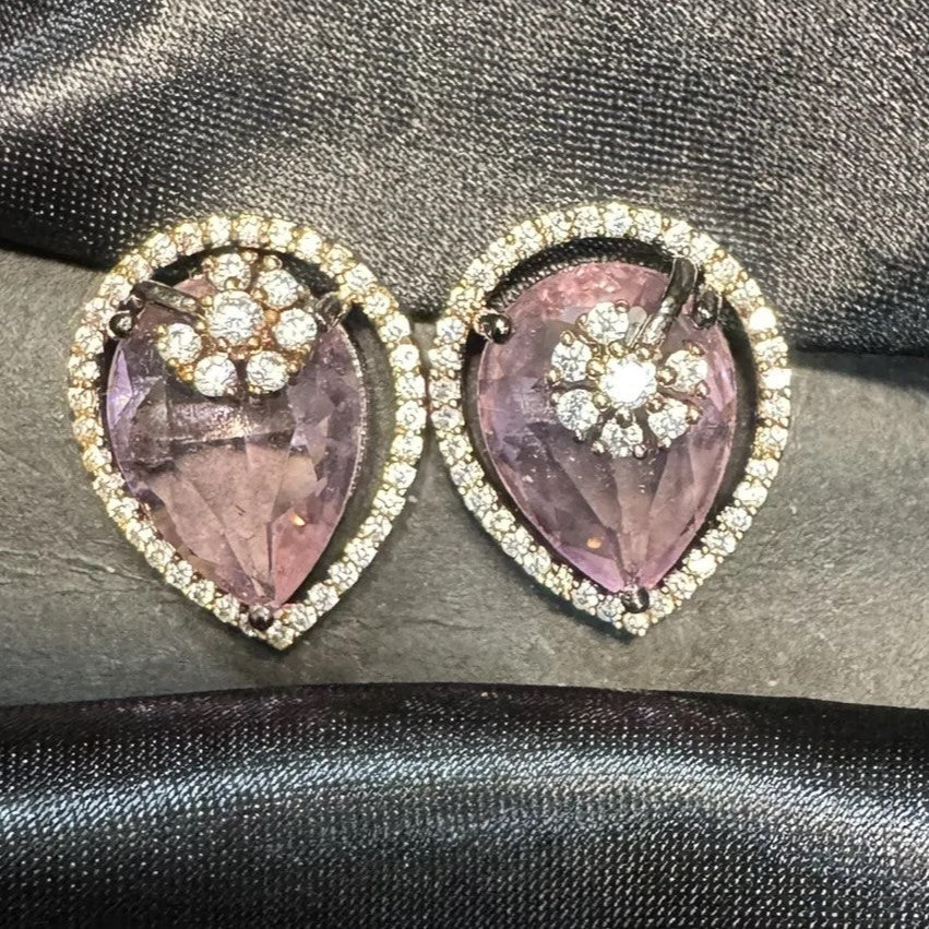 Teardrop shaped earrings with purple stones and American diamond accents on a dark fabric background