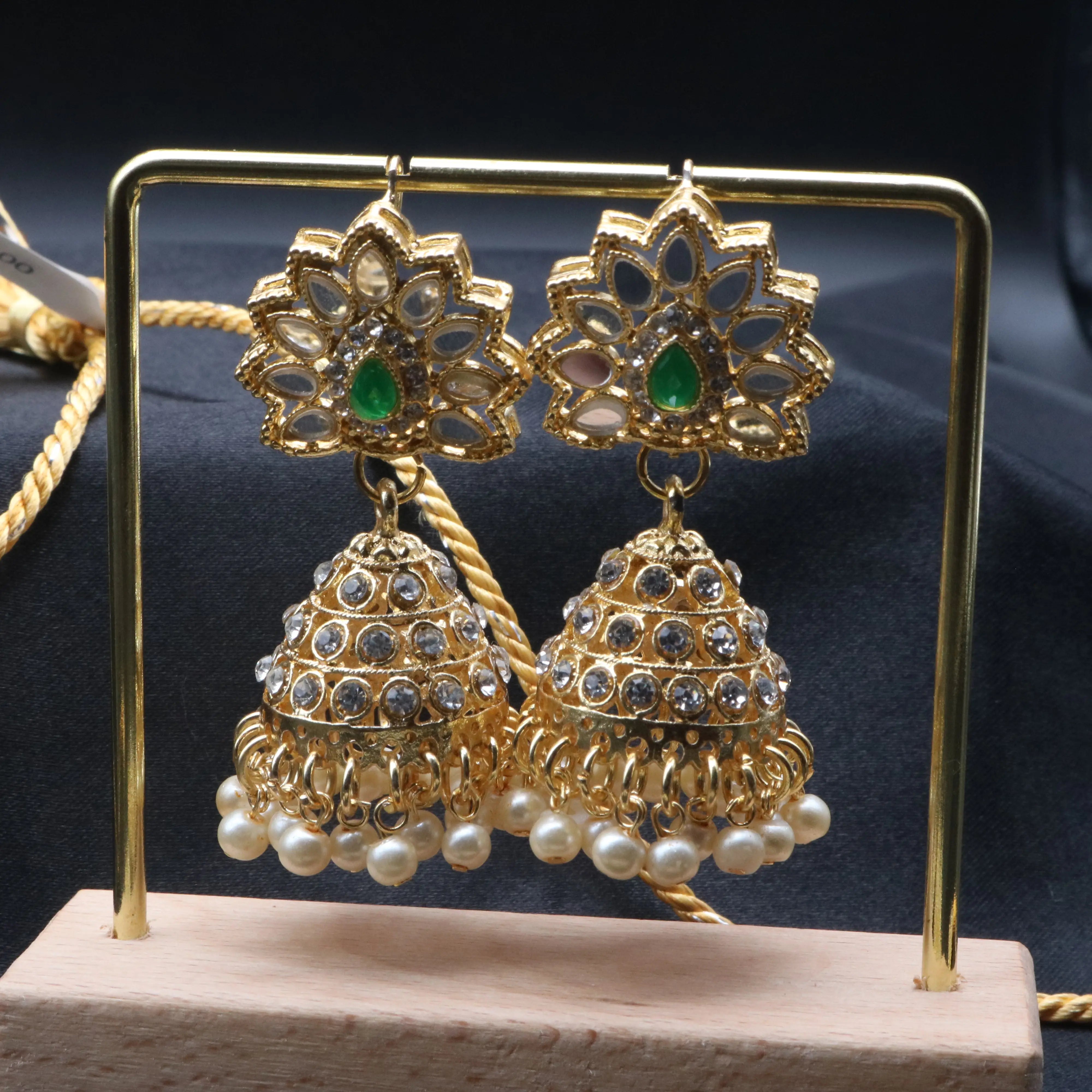 Detailed shot of Zinnia's gold jhumka earrings with mirror and emerald accents