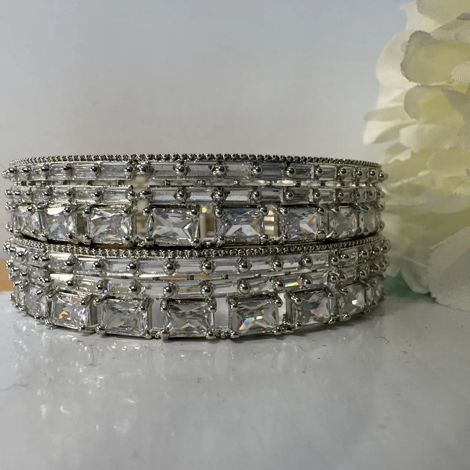 stainless steel bangles adorned with shimmering American diamonds and clear gemstones on a light gray surface with a white flower in the background