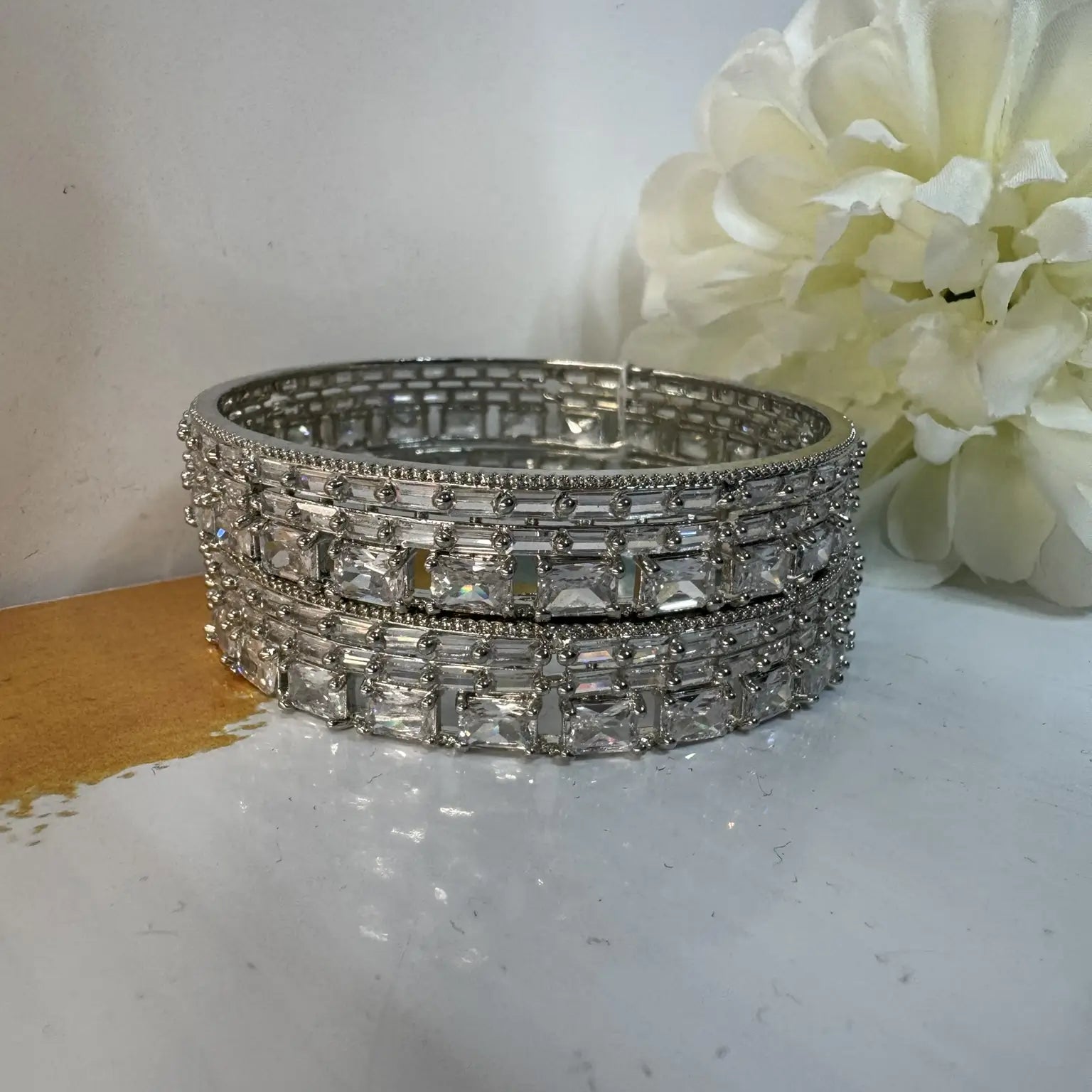 stainless steel bangles adorned with shimmering American diamonds and clear gemstones on a white surface with a white flower in the background