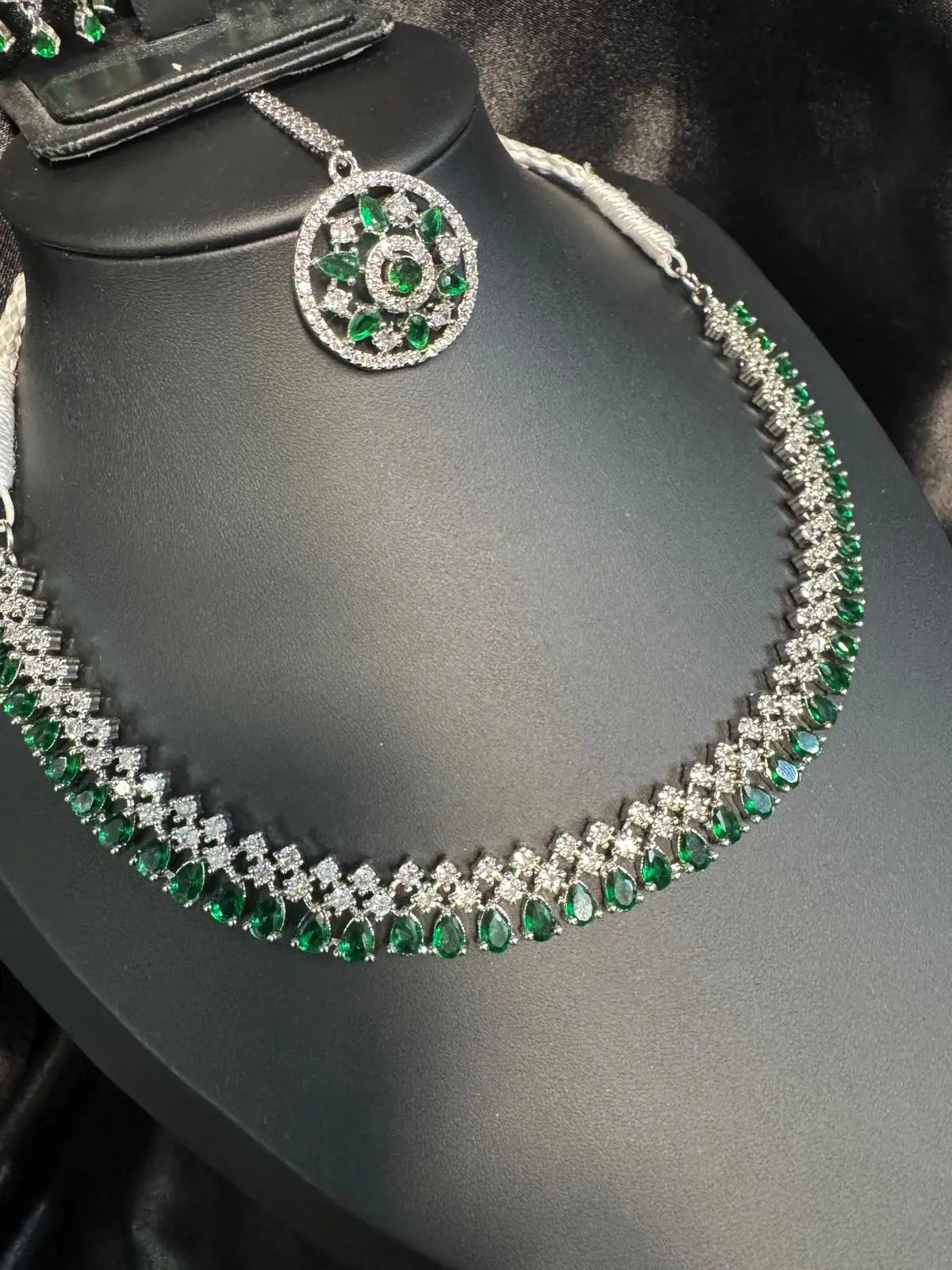 Close-up of Ameerah necklace featuring emerald green CZ teardrop stones and a circular pendant on black display stand.
