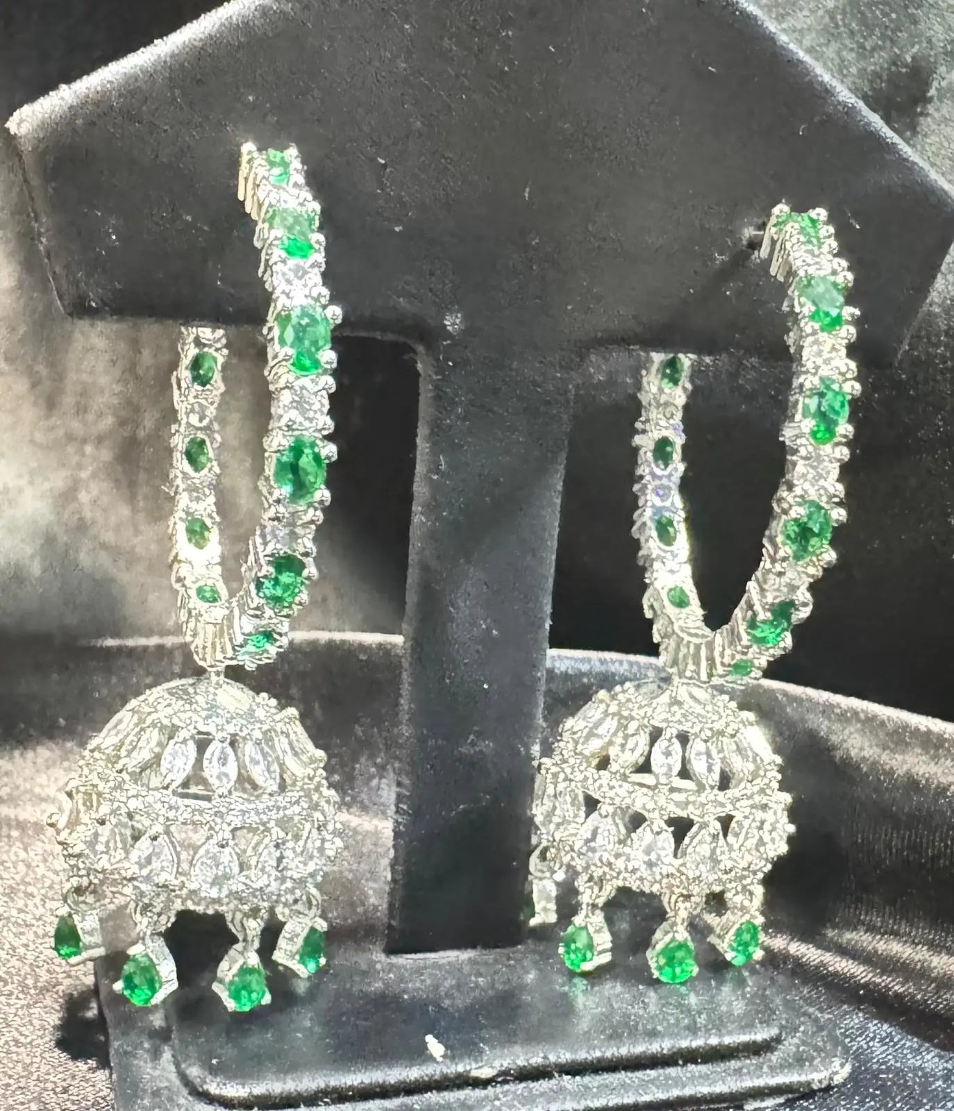 Close-up of jhumka-style earrings from the Ameerah set with intricate silver-tone detailing and dangling green CZ drops.