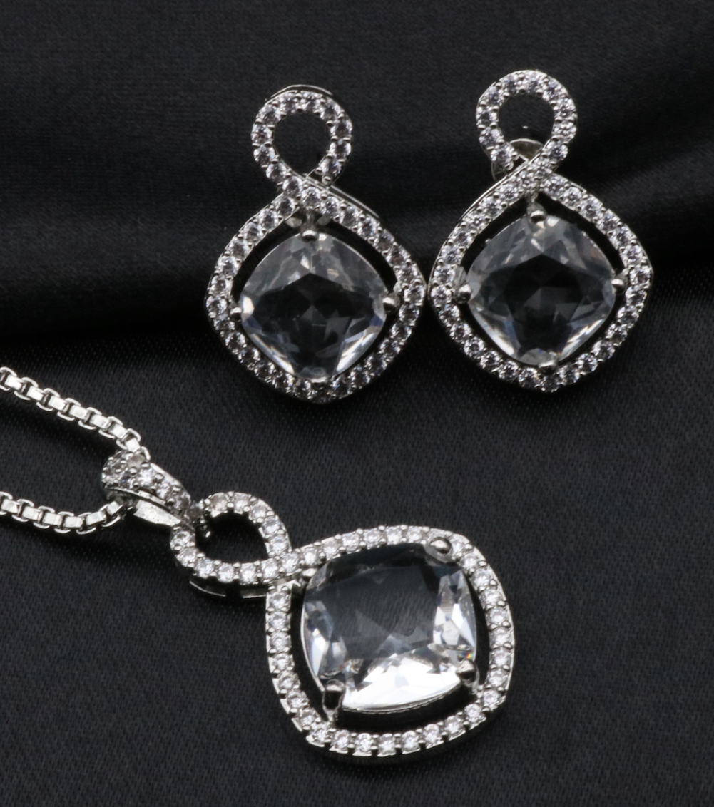A set of stainless steel jewelry, featuring a necklace and earrings with American diamond accents, displayed on a black background.