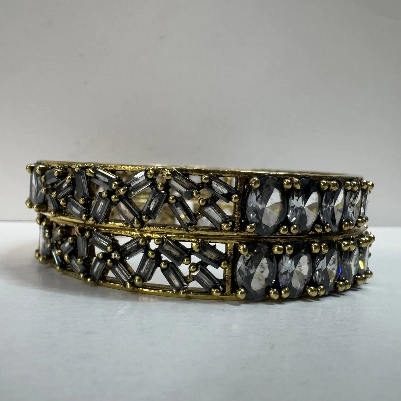 Pair of gold and black beaded bangles with black gemstones on a light gray background