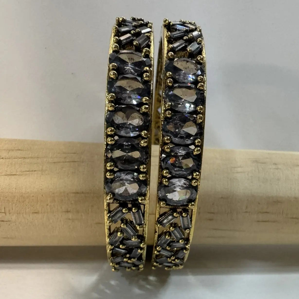 Pair of gold and black beaded bangles with gemstones wooden stick against a gray background