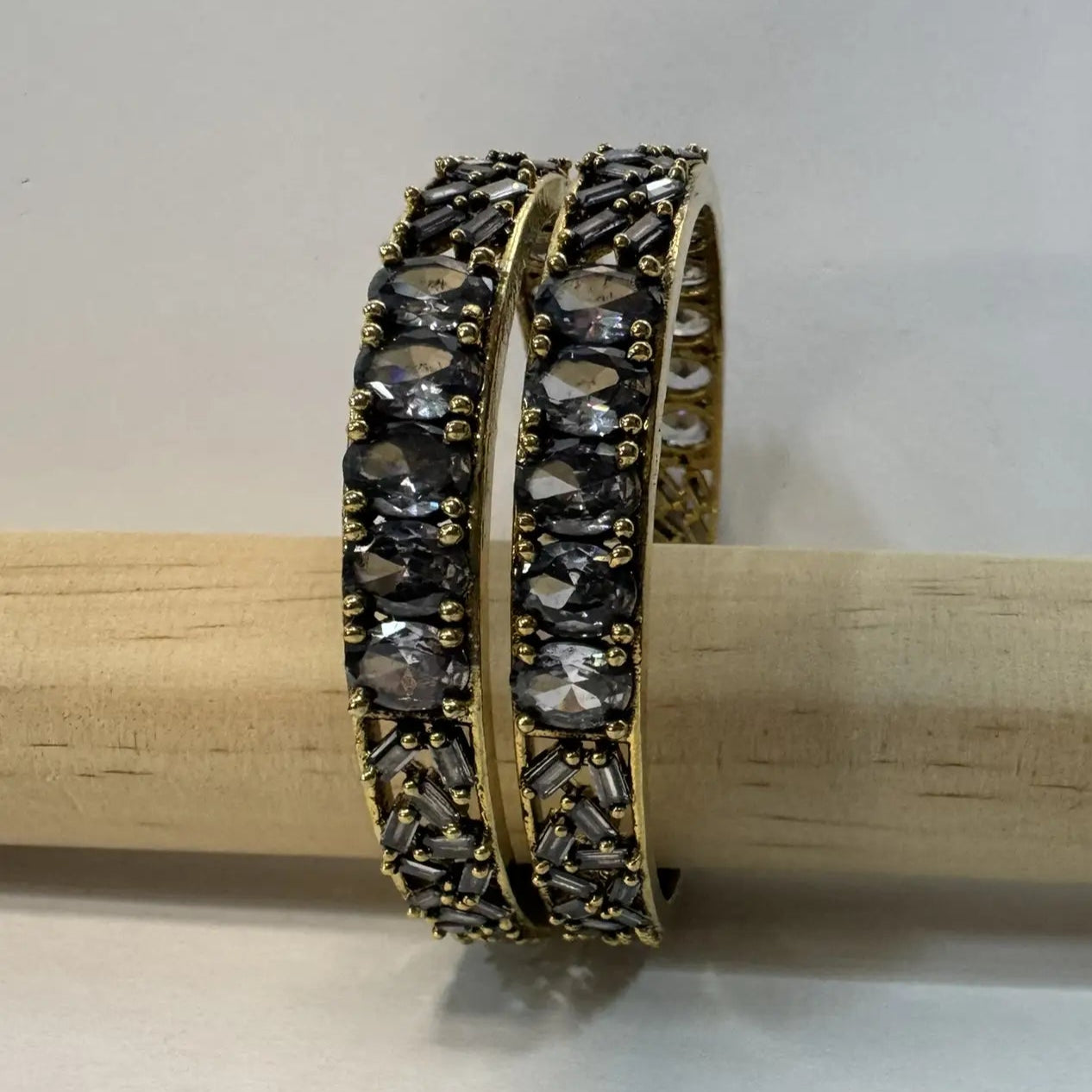 side view of Pair of gold and black beaded bangles with gemstones on a wooden stick against a white background
