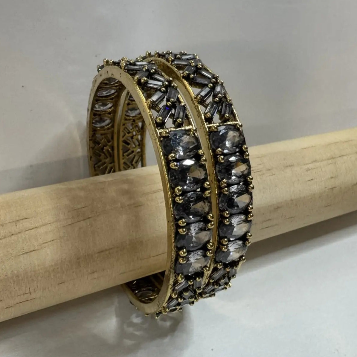 Pair of gold and black beaded bangles with gemstones on a wooden stick against a plain background
