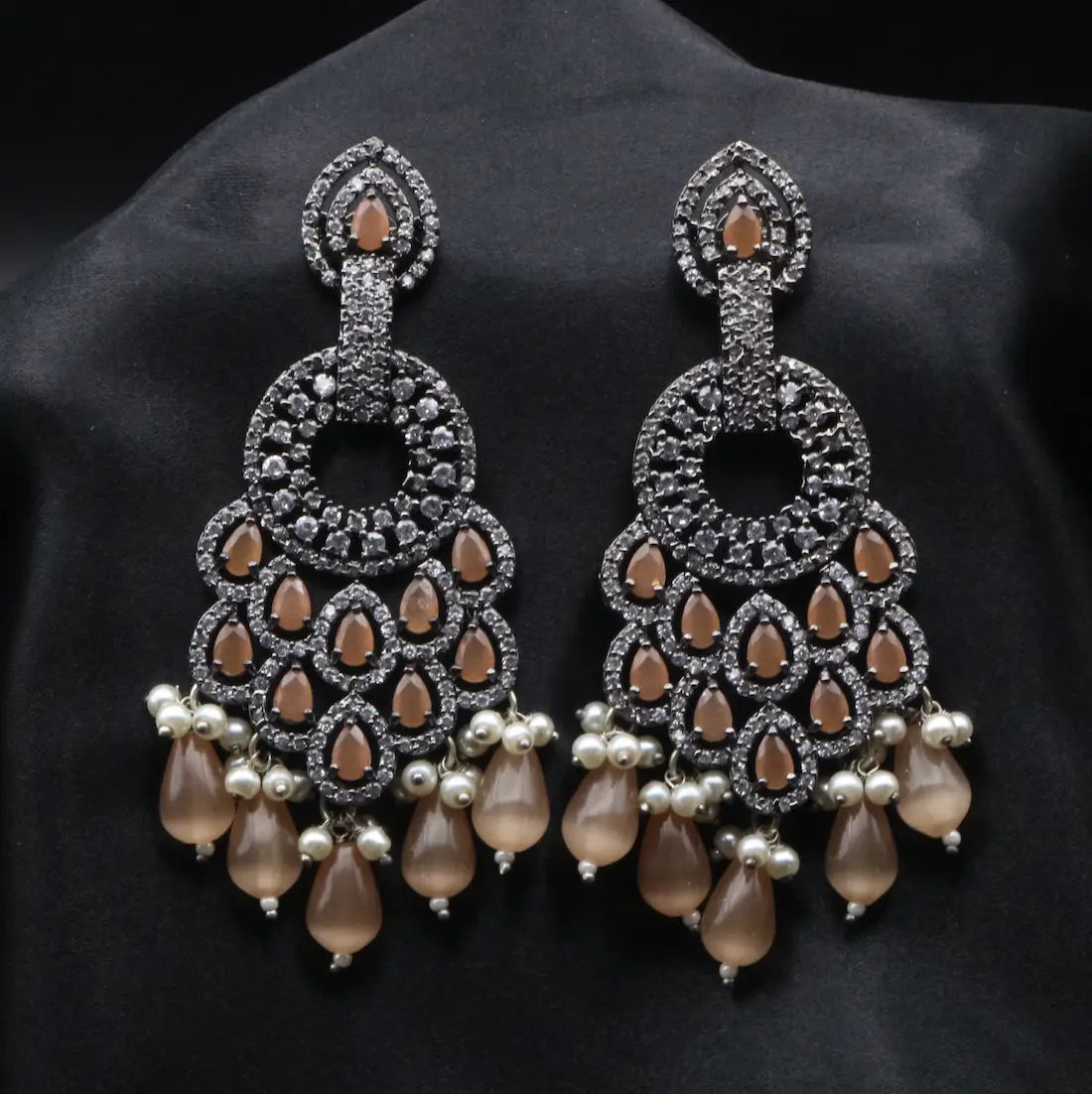 Pair of ornate earrings with orange teardrop stones and pearl-like beads on a black background
