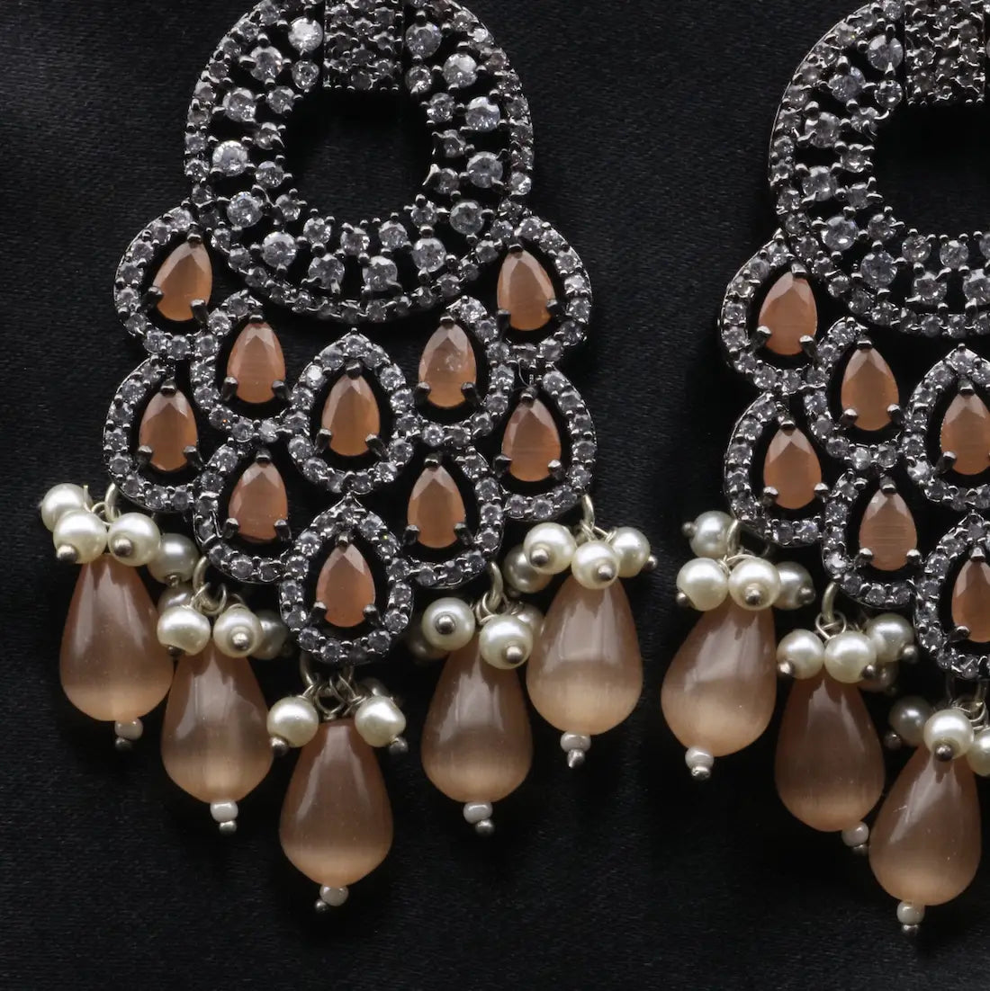 Ornate earrings with teardrop-shaped beads and pearl-like elements on a dark background