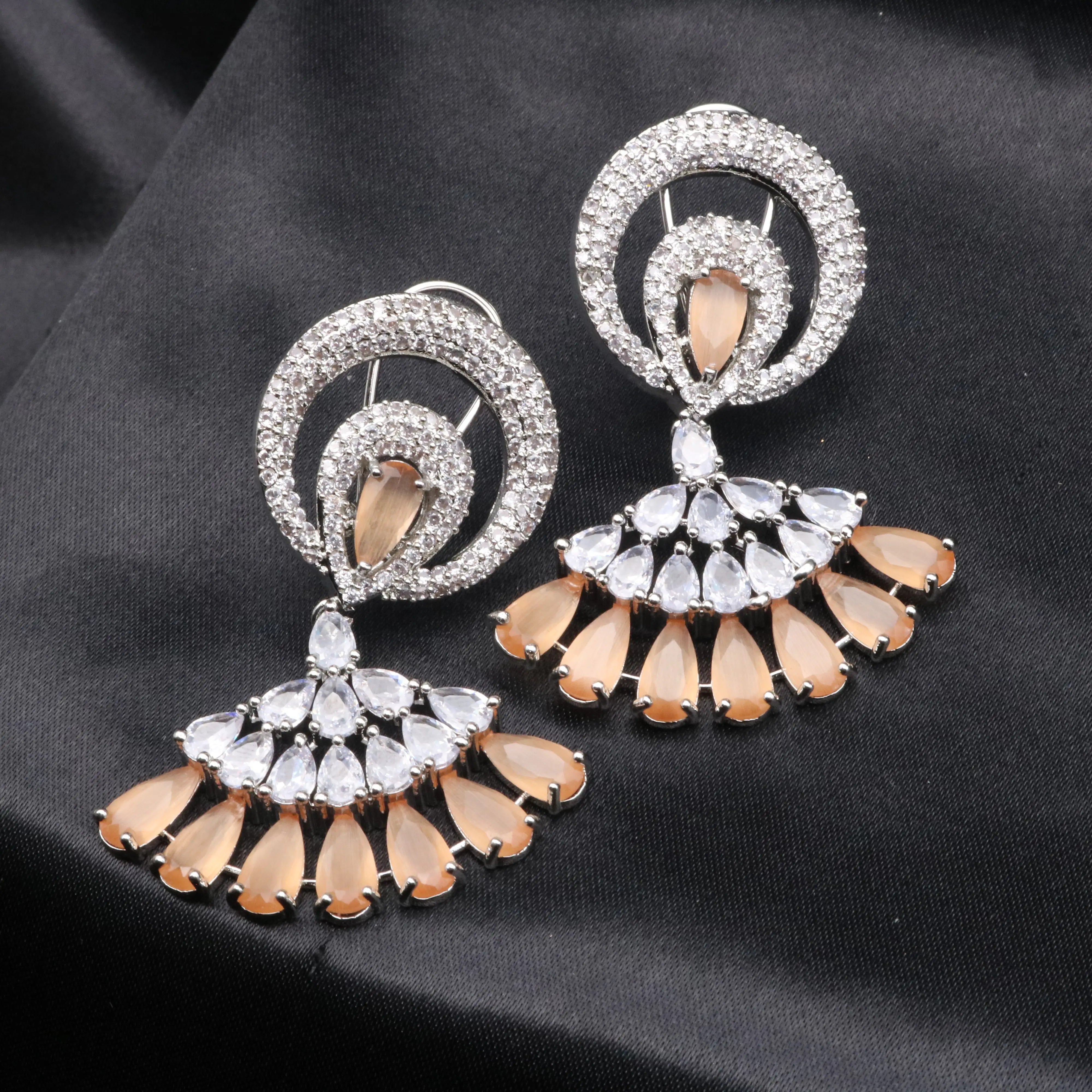 Ornate earrings with circular designs and peach-colored stones on a black background