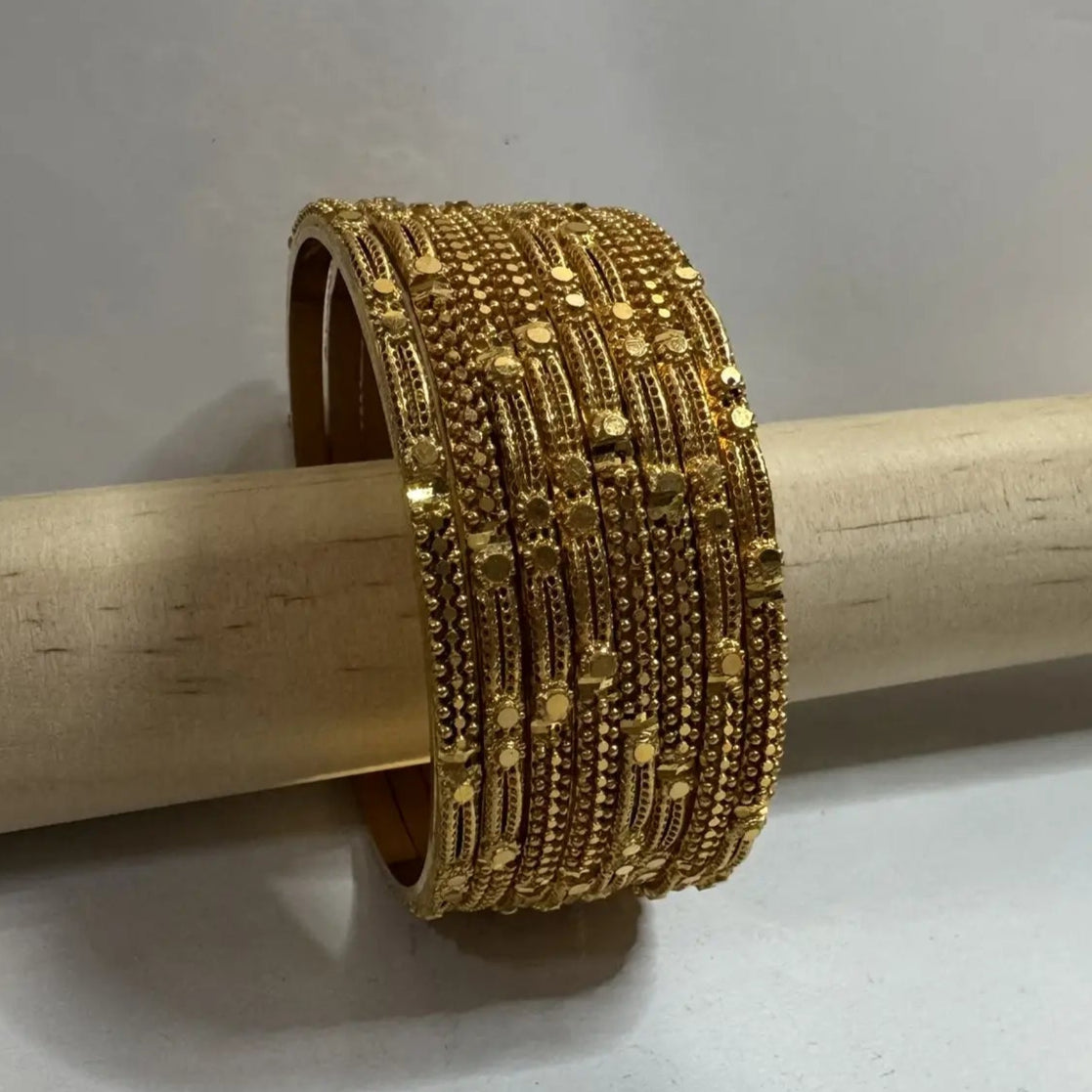 set of 8, 22k gold plated bangles on a on a wooden stick against a gray background