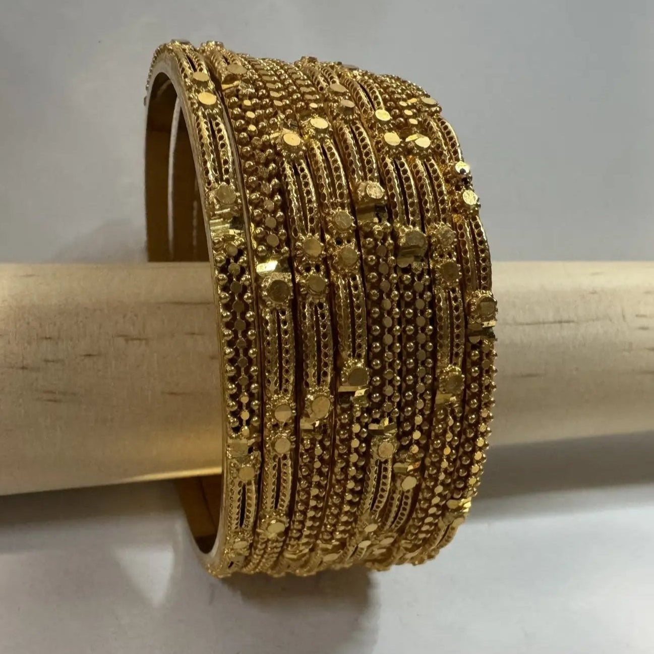 set of 8, 22k gold plated bangles with solid inside on a on a wooden stick against a gray background