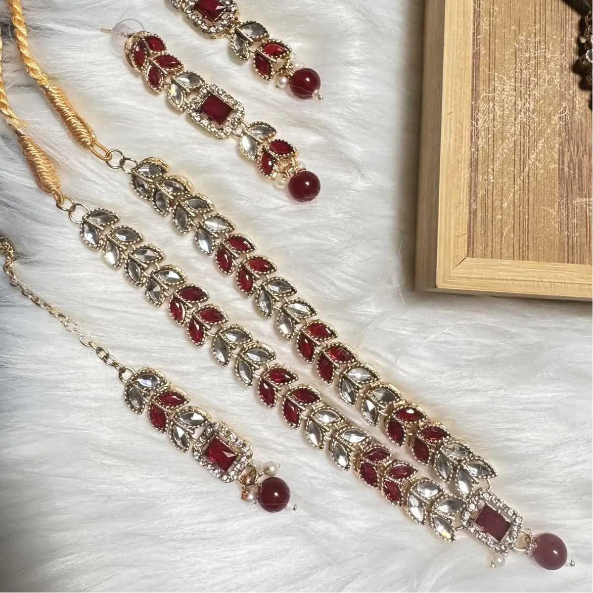 Full Bloom jewelry set in red and gold with leaf motif and pearl detailing on white fur background.